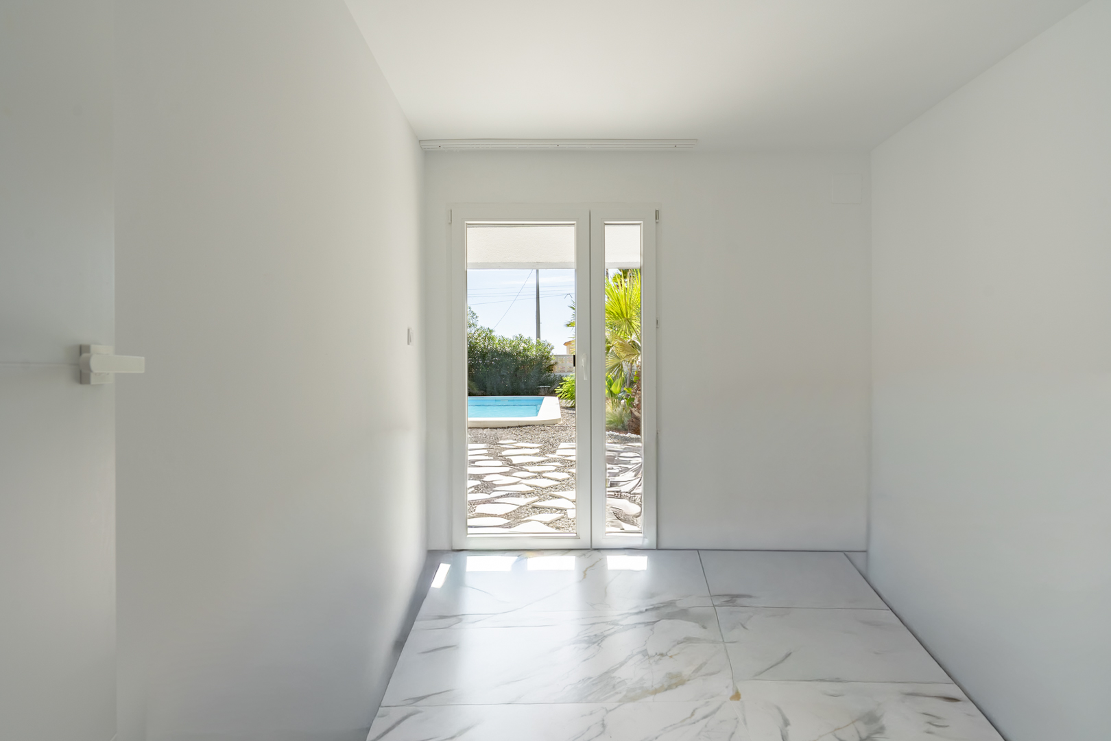 Bright room featuring marble-effect porcelain flooring and direct access to the pool terrace through a large glass door.