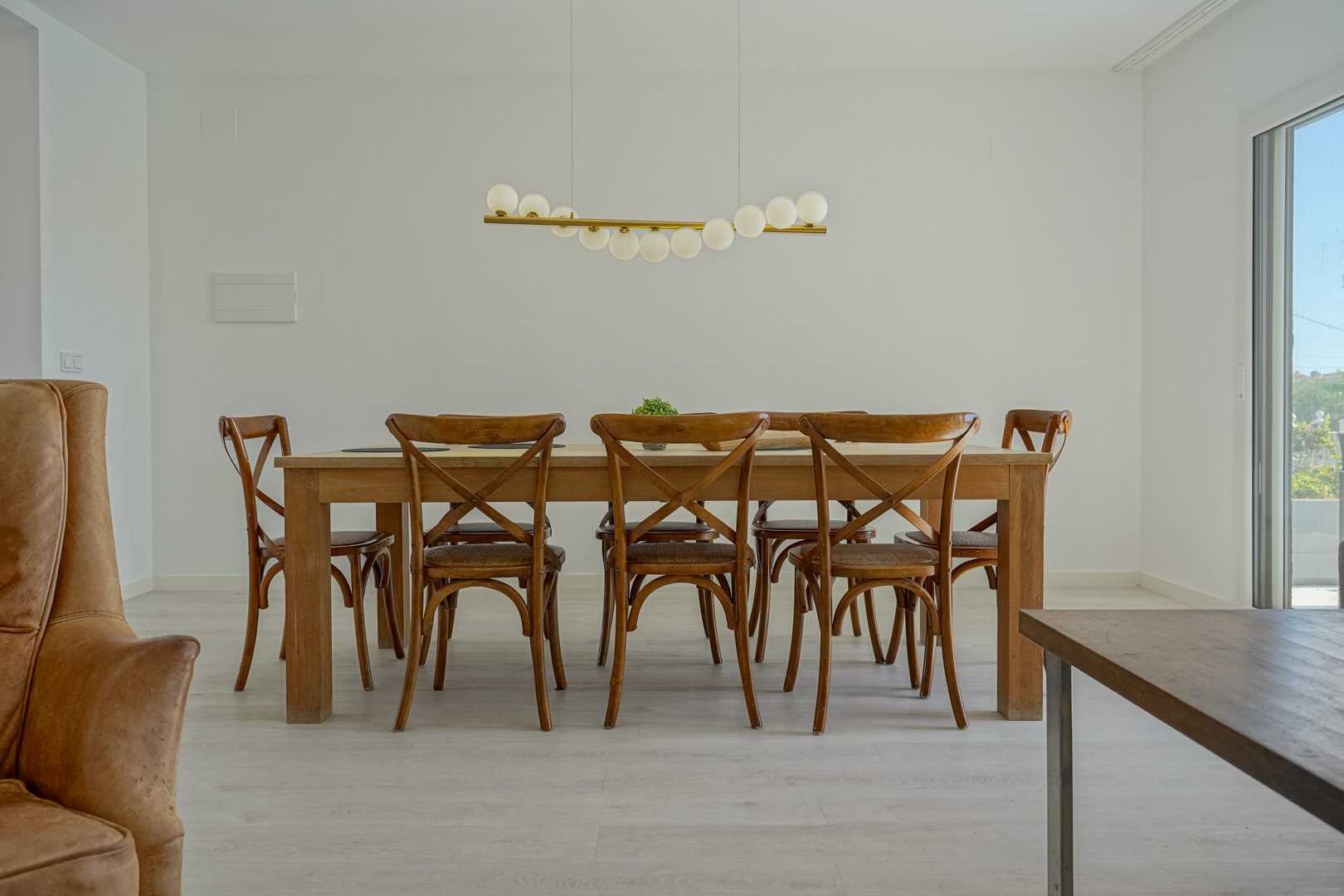 Dining area featuring a solid wood table and cross-back chairs, accented by a modern spherical pendant light and light-toned flooring.