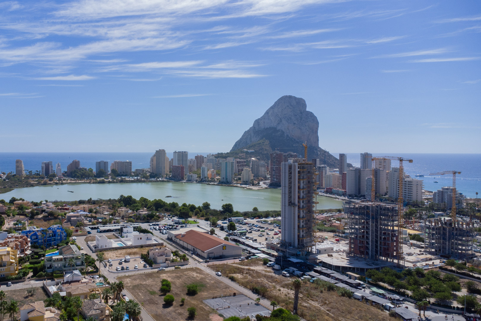 Elevated panoramic view of Calpe featuring the Peñón de Ifach, Las Salinas lagoon, and the coastal skyline under a clear blue sky.