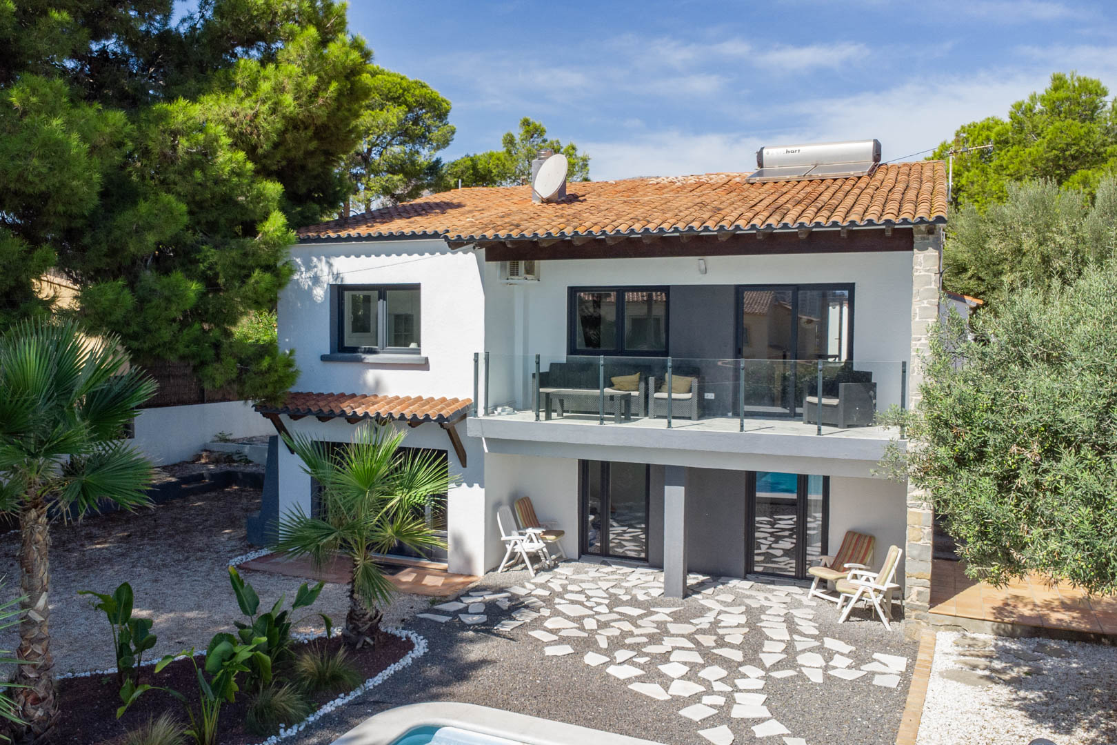 Exterior view of the two-story villa featuring a glass-railed terrace, solar water heater on the roof, and a stone-paved lower patio area.