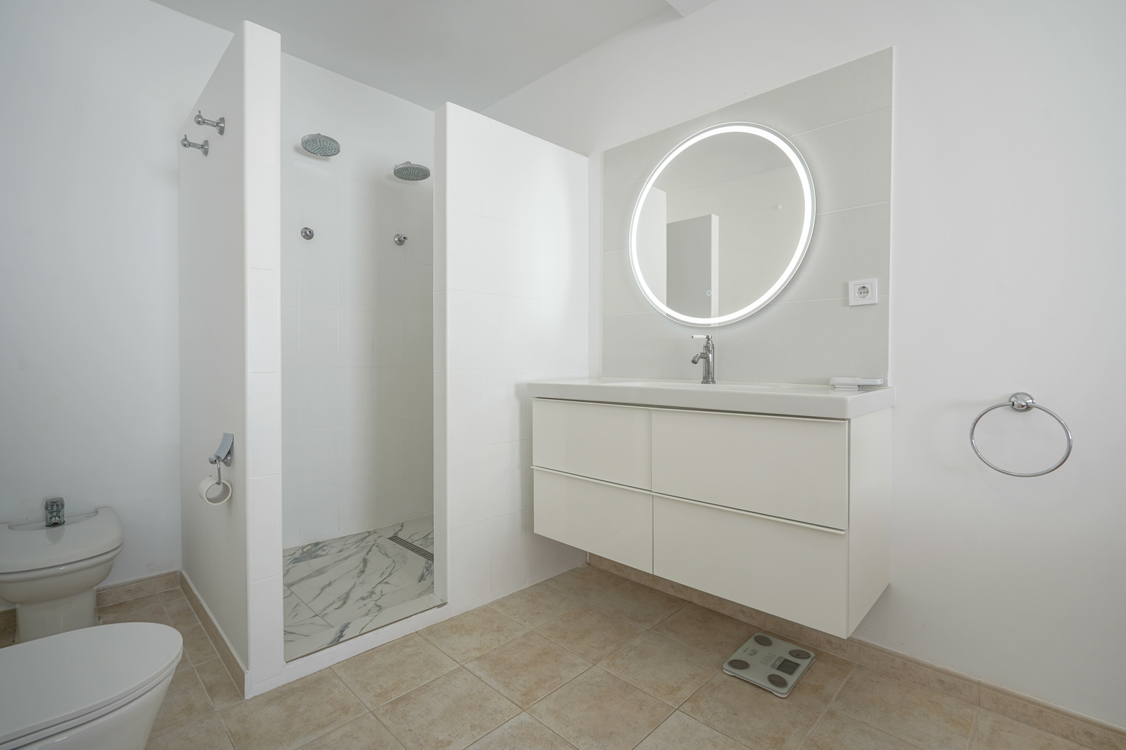 Modern bathroom featuring a floating white vanity, circular backlit LED mirror, and a spacious walk-in double shower with marble-effect flooring.