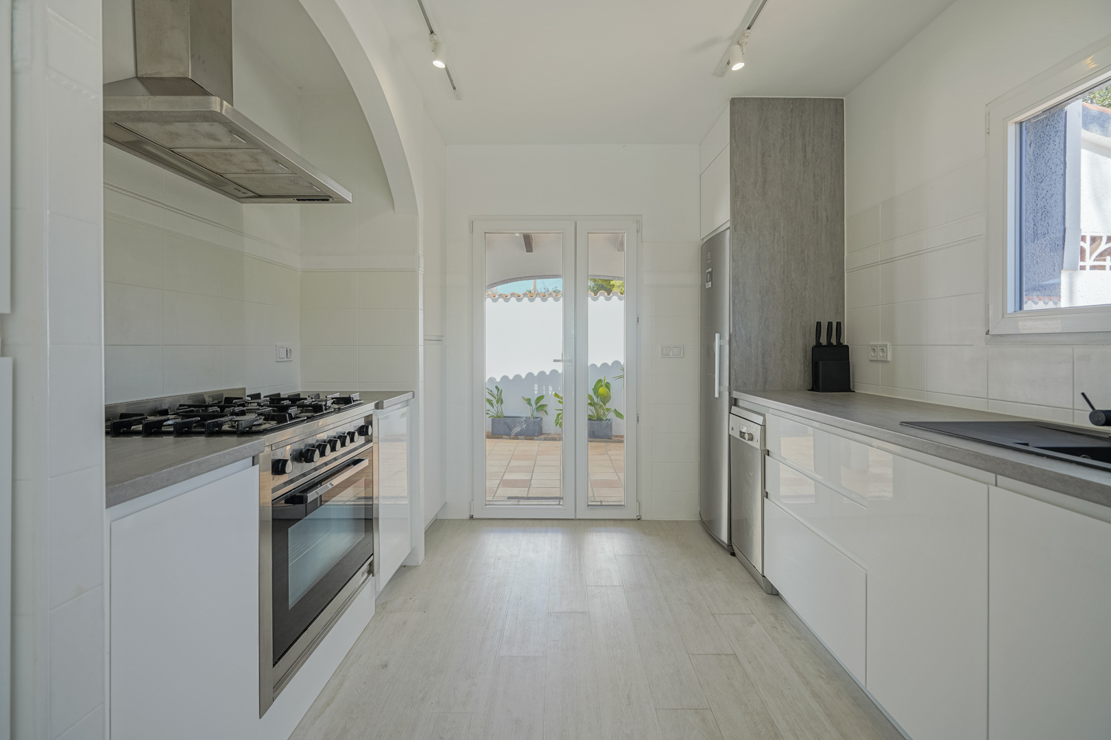 Modern kitchen featuring glossy white cabinetry, grey countertops, and stainless steel appliances. It includes a gas range and direct access to the outdoor terrace.