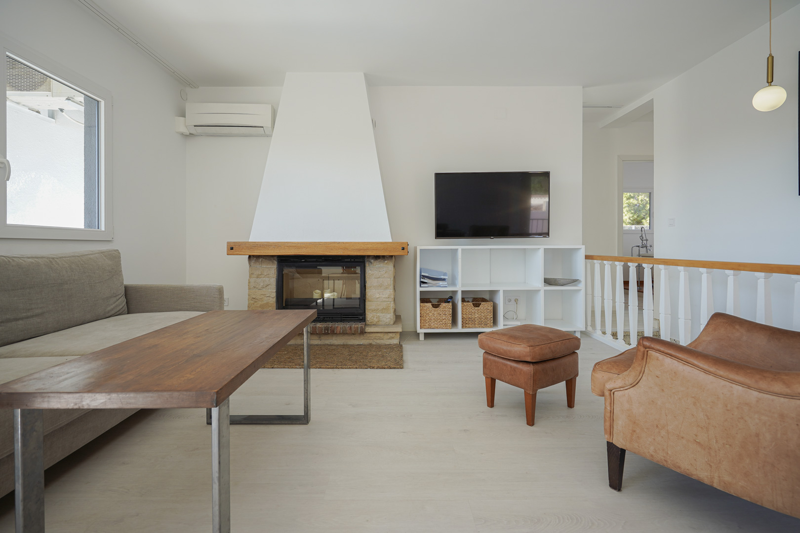 Modern living area featuring a stone fireplace with a wooden mantel, light wood-effect flooring, and a wall-mounted TV adjacent to the staircase.