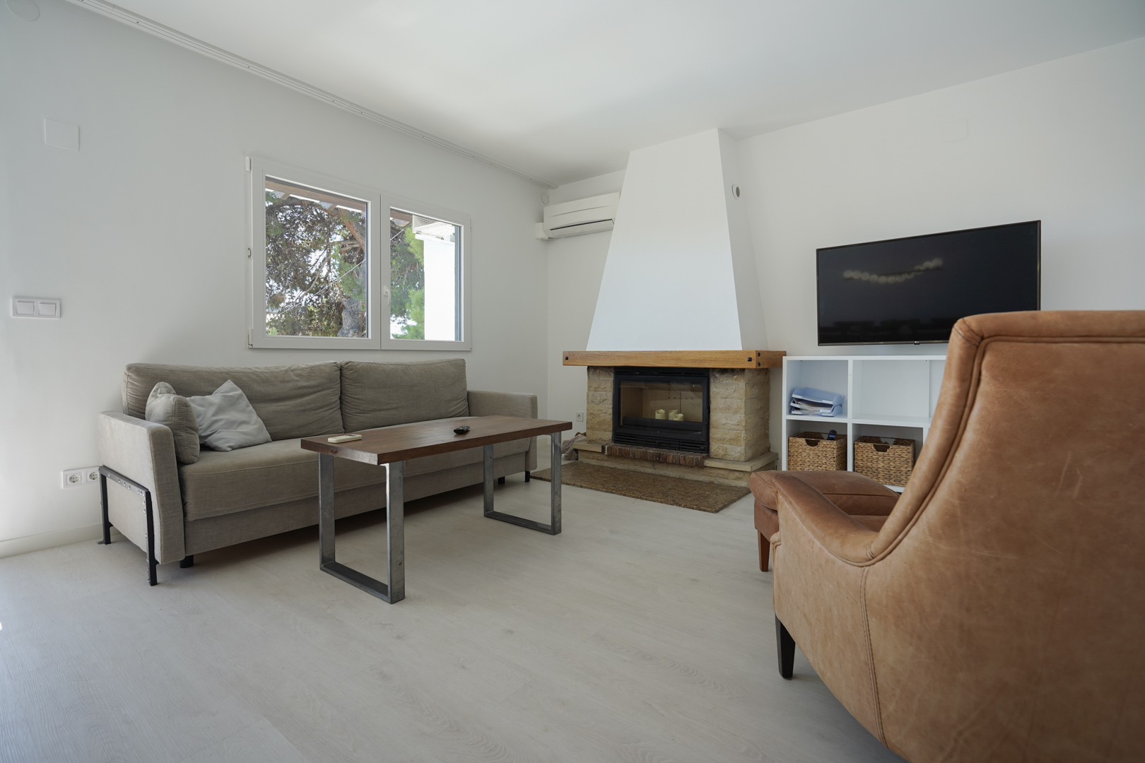 Modern living area featuring a stone fireplace with wooden mantel, leather armchair, and grey sofa. Equipped with split-system air conditioning and double-glazed windows.