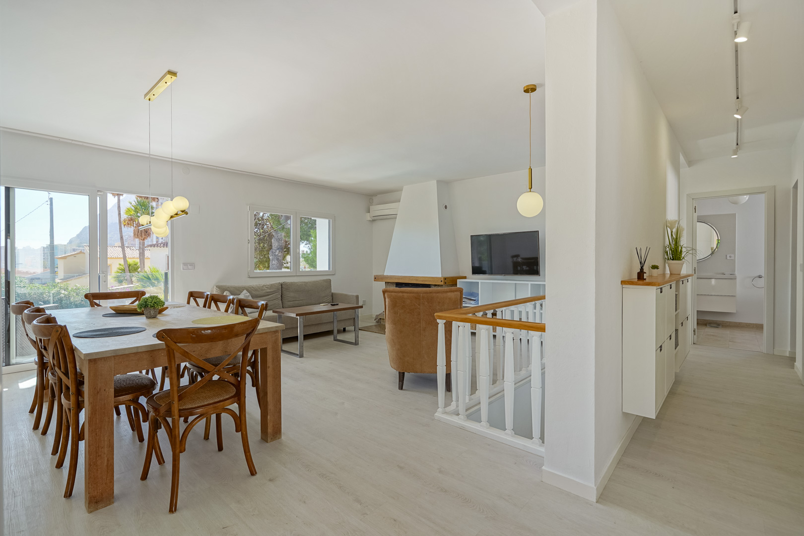Open-plan living and dining space featuring a white fireplace, light wood-effect flooring, and sliding doors opening to a terrace with Peñón de Ifach views.
