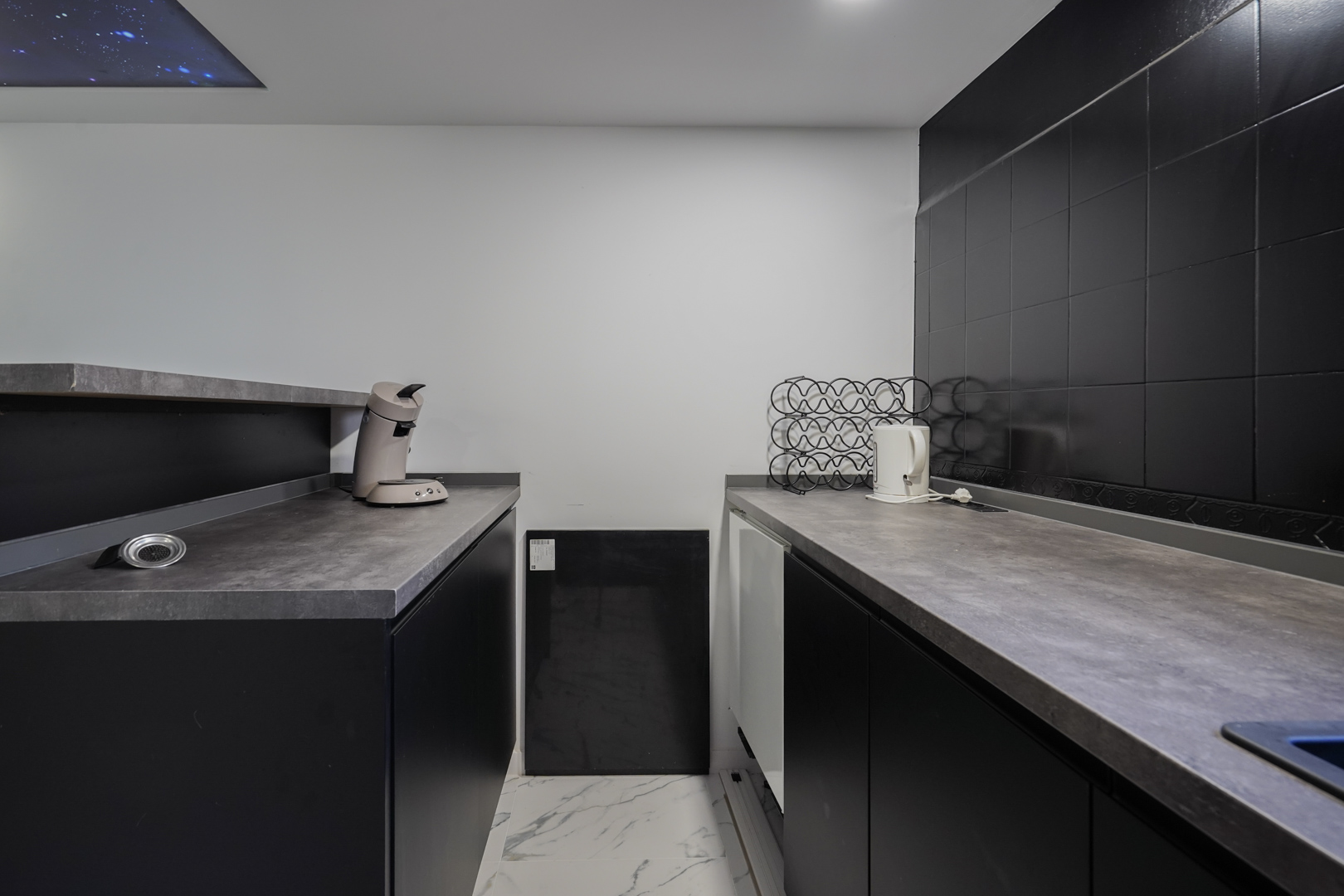 Secondary kitchen area featuring black cabinetry, grey stone-effect countertops, and marble-look flooring. A decorative starry sky ceiling panel adds a unique touch.