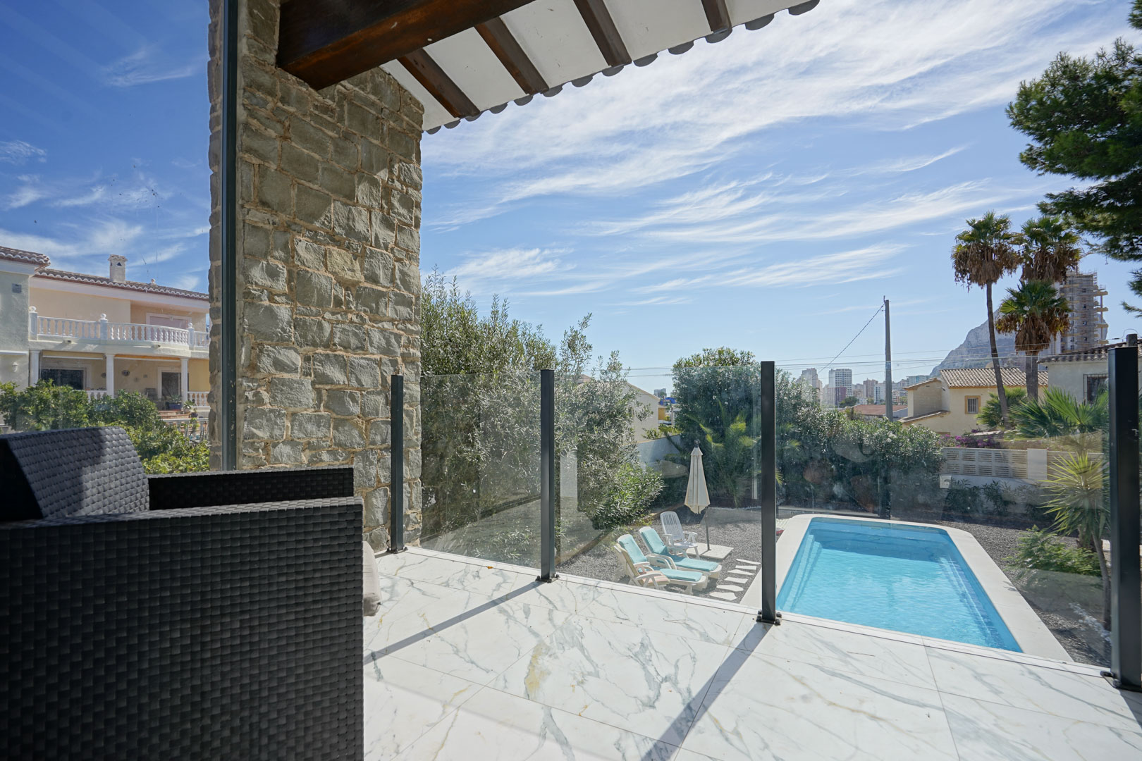 Upper terrace featuring marble-effect tiling, glass railings, and views over the private pool, garden, and the iconic Peñón de Ifach.