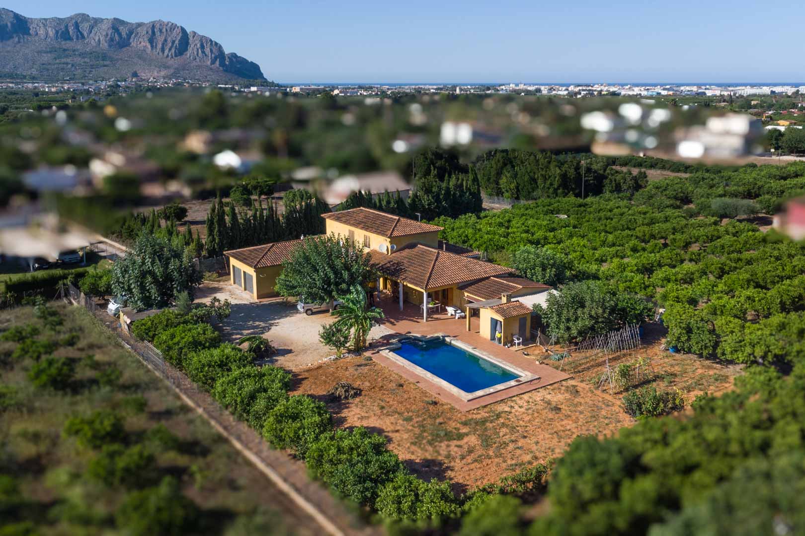 Aerial perspective of the Mediterranean villa featuring a private pool and extensive orchards, with Mount Segaria and the sea visible in the background.