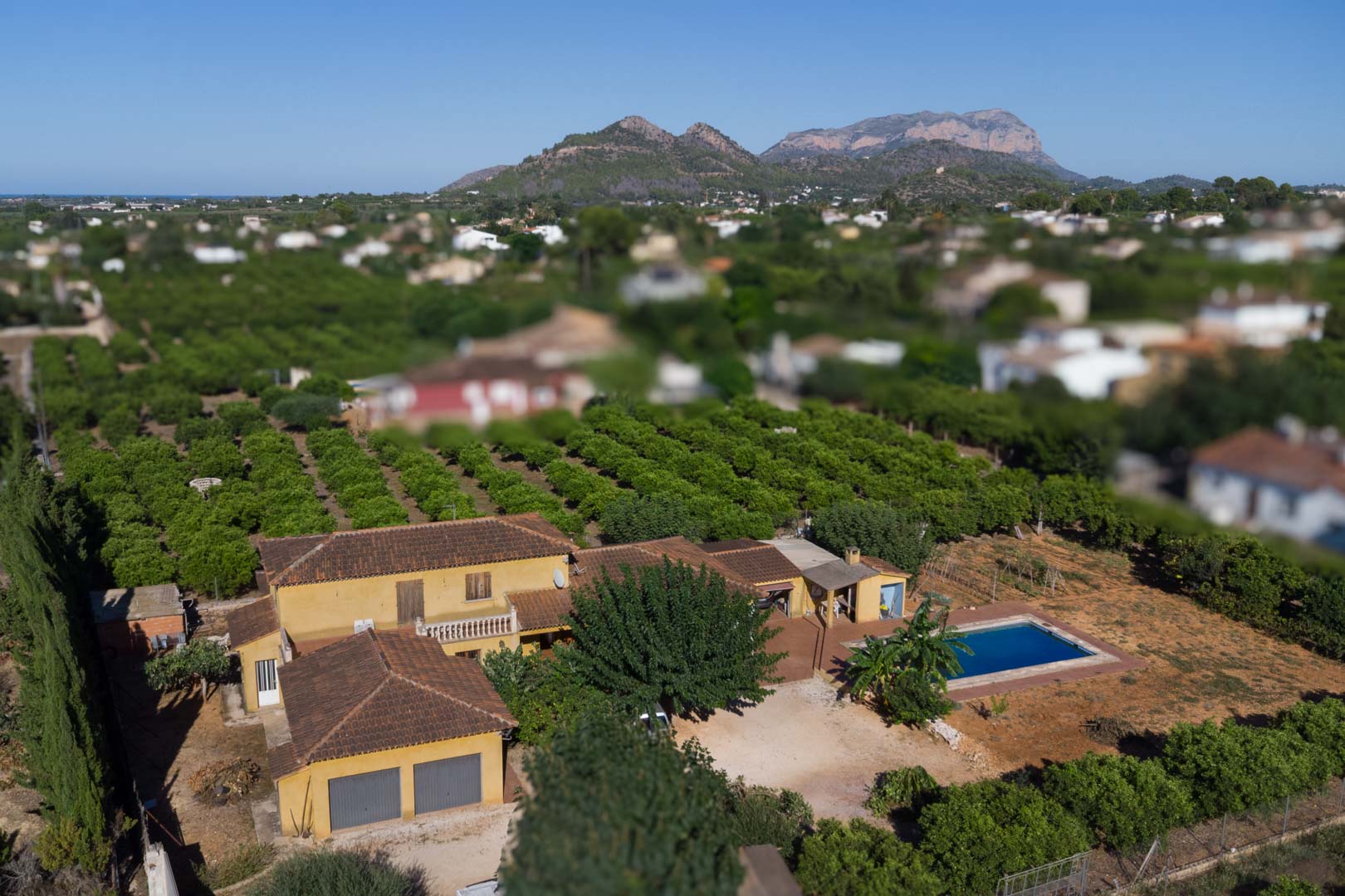 Aerial view of the rustic villa featuring a private swimming pool, extensive citrus orchards, and panoramic views of the Segaria mountain range.