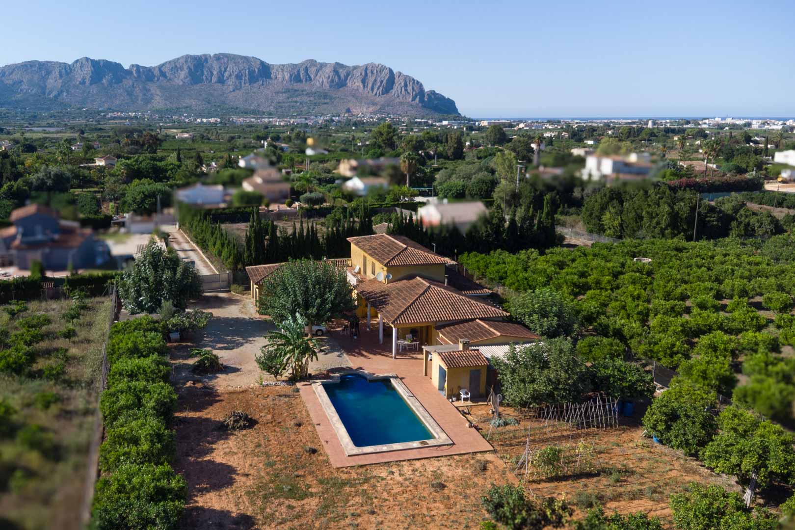 Aerial view of the villa featuring terracotta roofing, a private swimming pool, and expansive citrus orchards set against the Segaria mountain range.