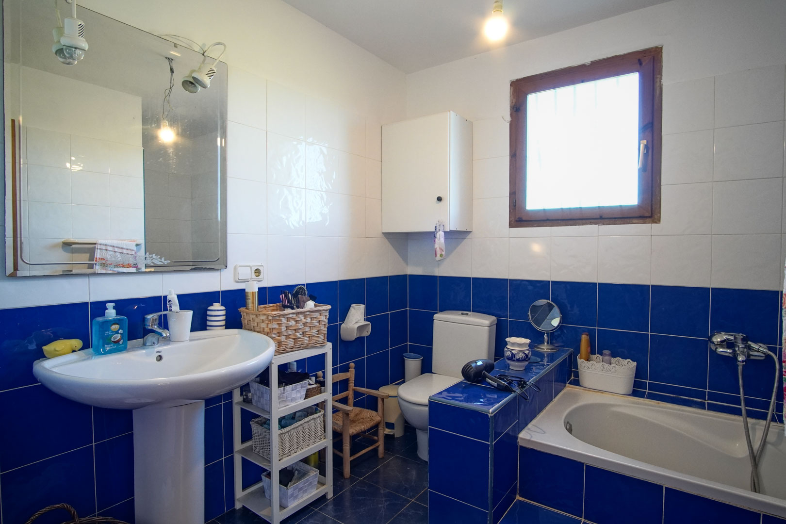 Bathroom featuring blue and white tiling, a pedestal sink, a built-in bathtub, and a wooden-framed window providing natural ventilation.