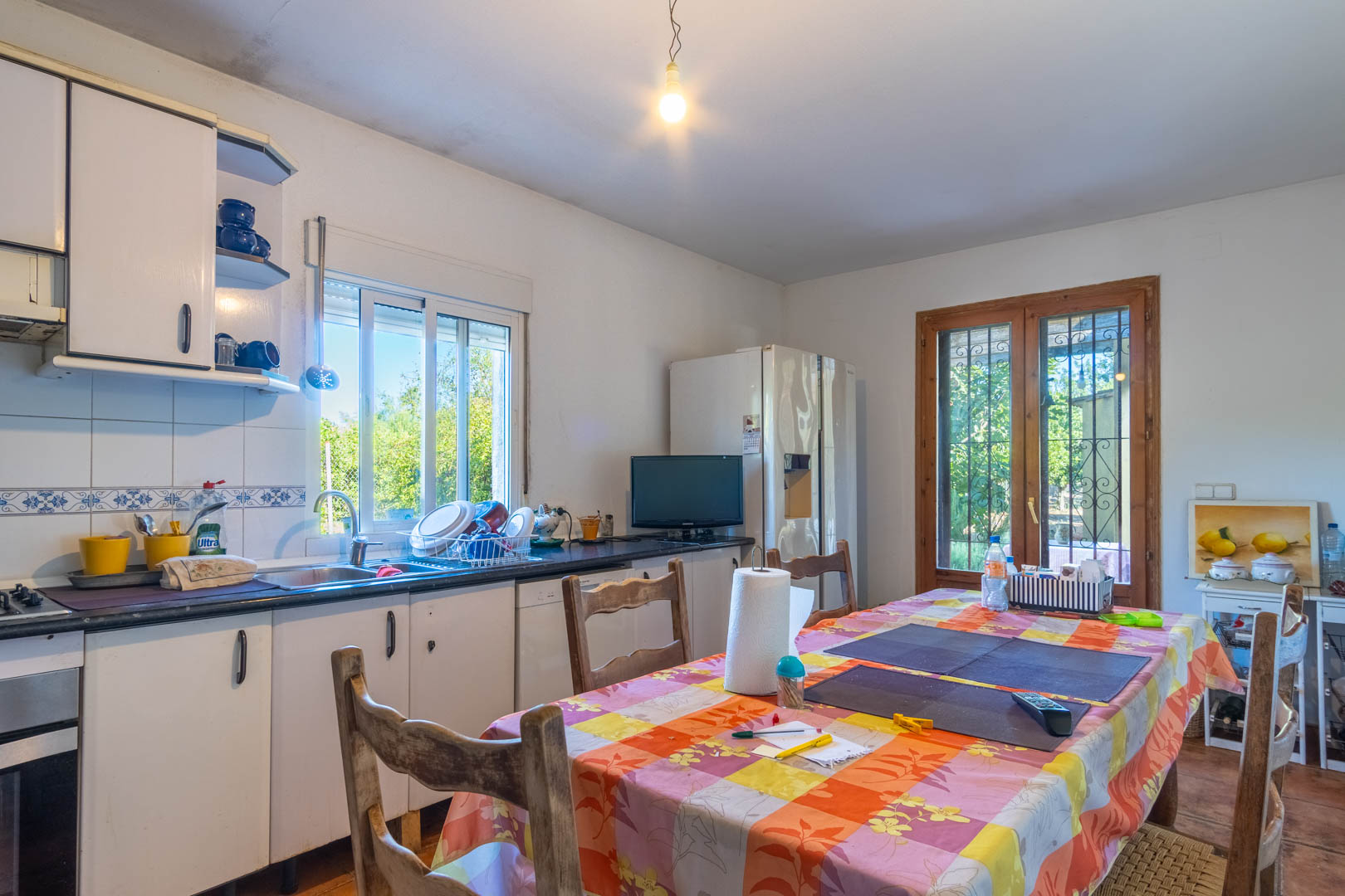 Functional kitchen featuring white cabinetry, dark countertops, and a dining area. It offers direct outdoor access and garden views through wooden-framed glass doors.