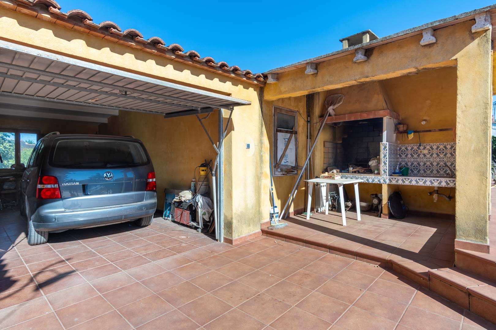 Functional outdoor area featuring a covered parking space and a traditional built-in barbecue with a tiled backsplash and sink.