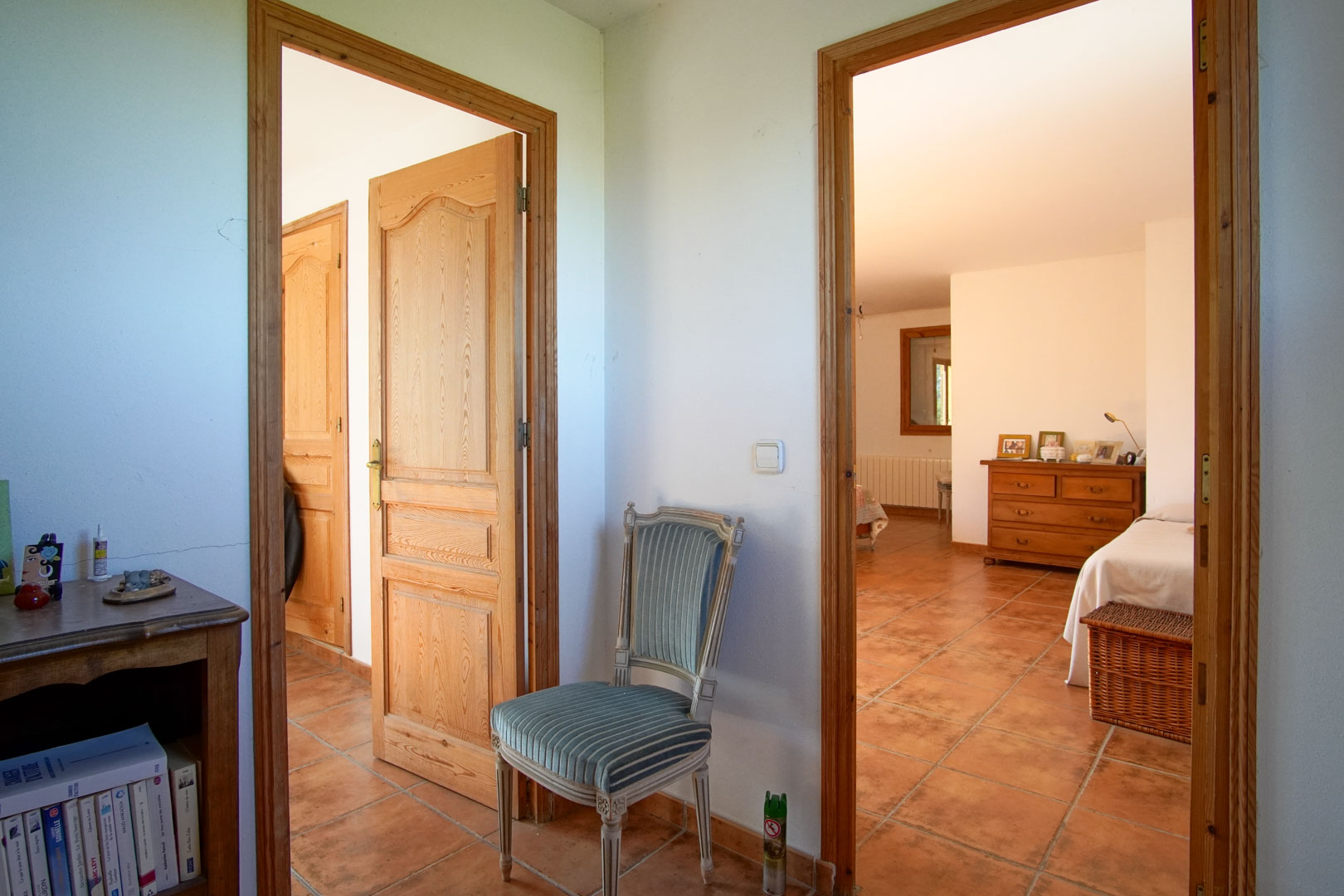 Hallway featuring rustic terracotta tile flooring and solid wood doors, providing access to bright bedrooms with traditional furnishings and natural light.