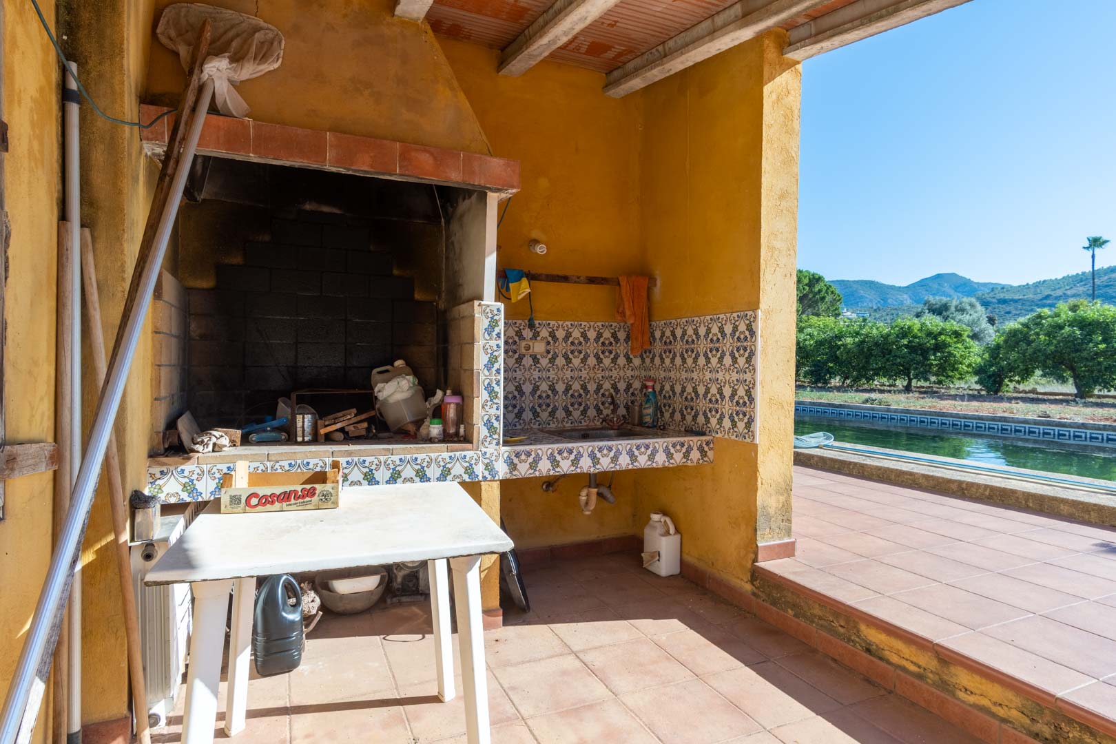 Outdoor kitchen featuring a built-in barbecue, traditional tiled backsplash, and sink, overlooking the private pool and Segaria mountain range.