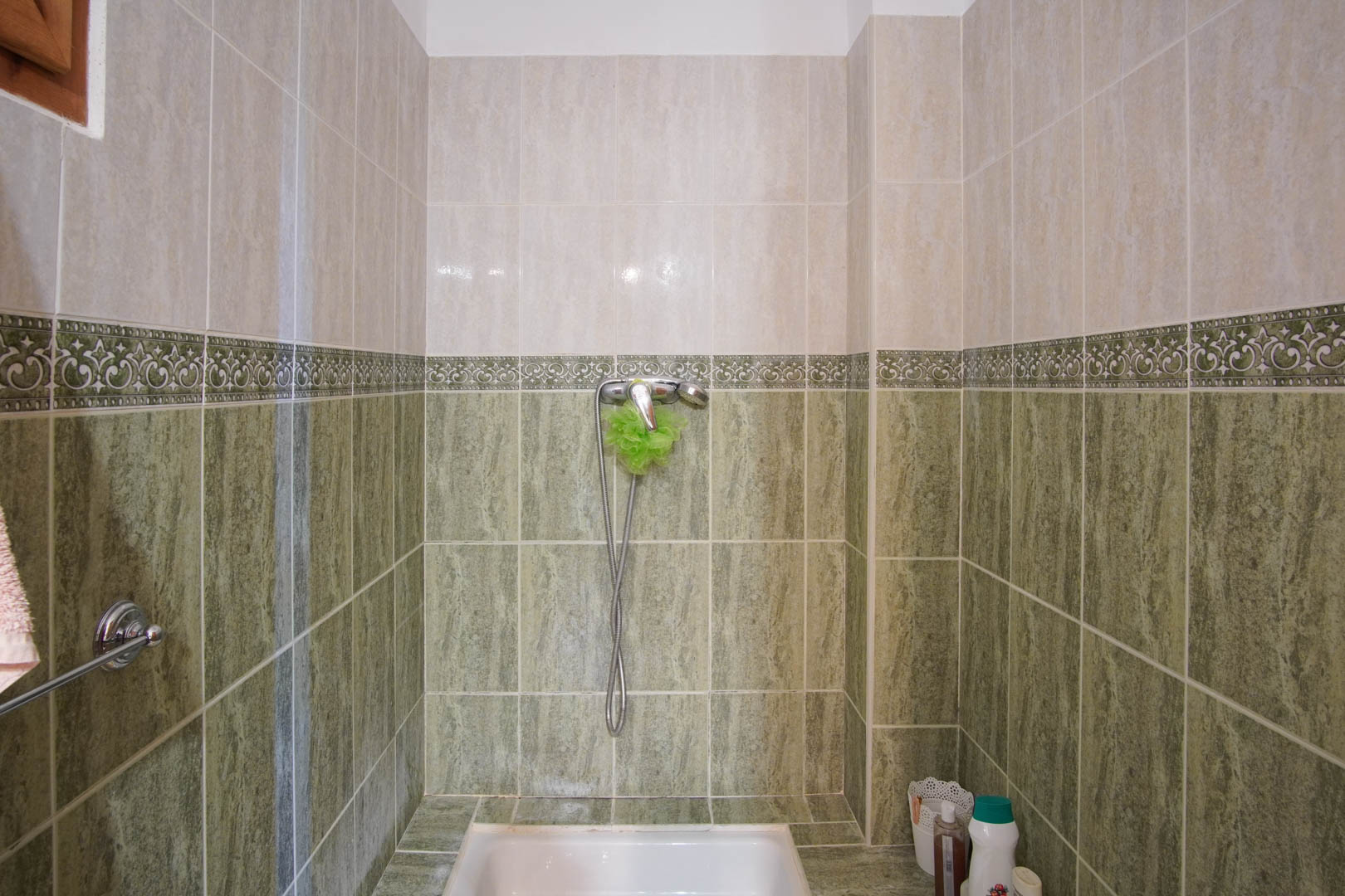 Shower area featuring two-tone ceramic tiling in green and cream, separated by a decorative border. Equipped with a white shower tray and chrome fixtures.