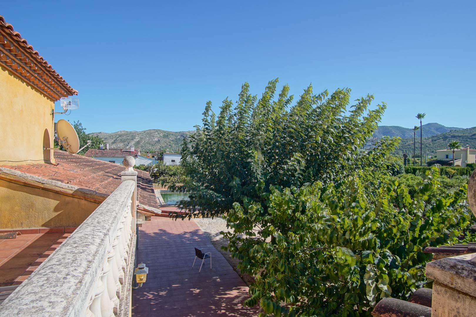 View from the upper terrace with a stone balustrade, overlooking the tiled patio, private pool, and mature trees with the Segaria mountains in the distance.