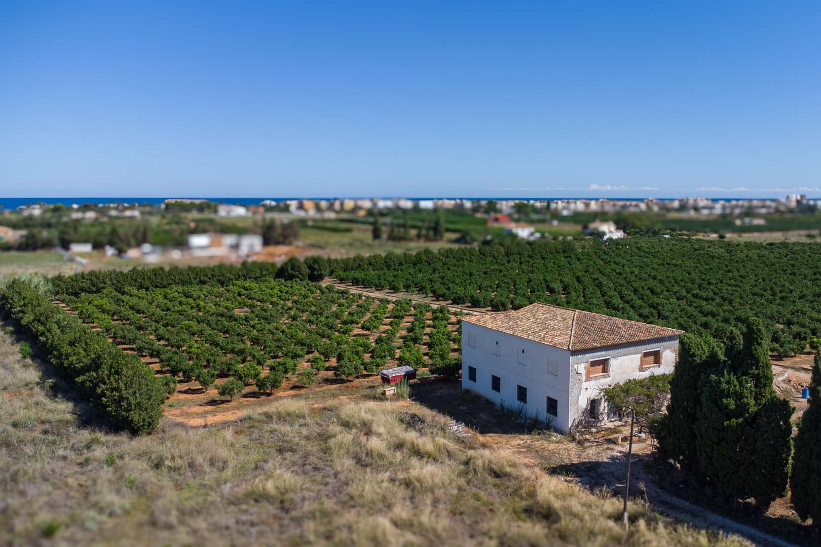 Aerial view of the country house surrounded by citrus groves, featuring a white facade, tiled roof, and panoramic views of the Mediterranean Sea.