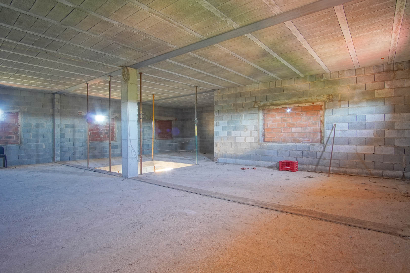 Open-plan interior in raw construction state featuring concrete block walls, steel beams, and a staircase opening, ready for custom layout design.