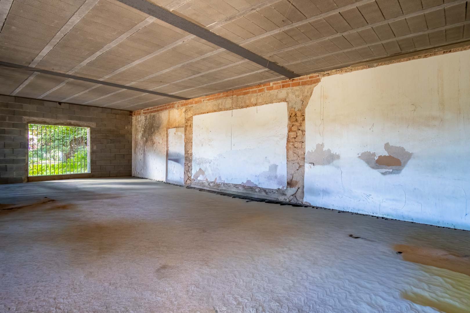 Open-plan interior space under renovation featuring concrete flooring, exposed ceiling beams, and walls showcasing a mix of original stone and brickwork.