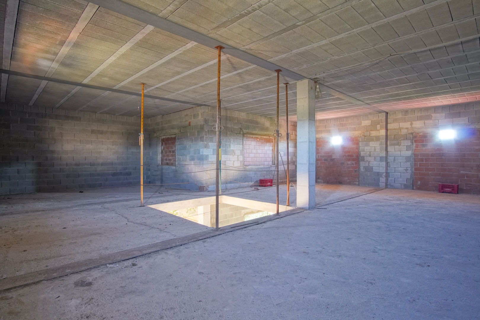 Open-plan upper floor under renovation featuring exposed concrete blocks, structural pillars, and a central opening for a future staircase.
