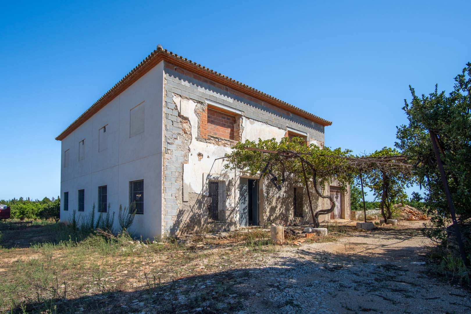 Two-story rural house under renovation featuring a traditional tile roof, original vine trellis, and a solid structure ready for custom finishing.