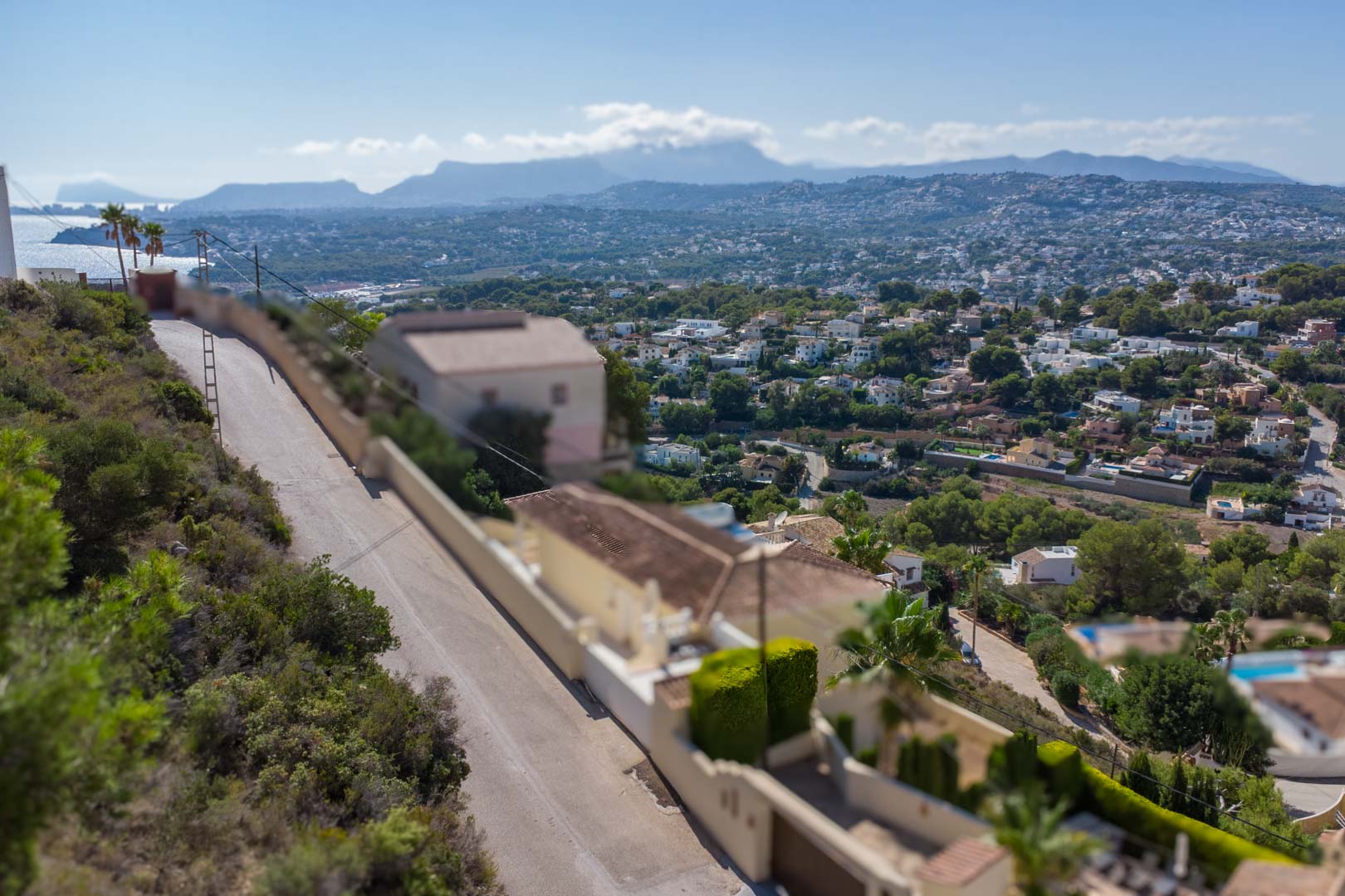 Elevated panoramic view from El Portet overlooking the Moraira coastline and Mediterranean Sea, with mountain ranges visible in the distance.