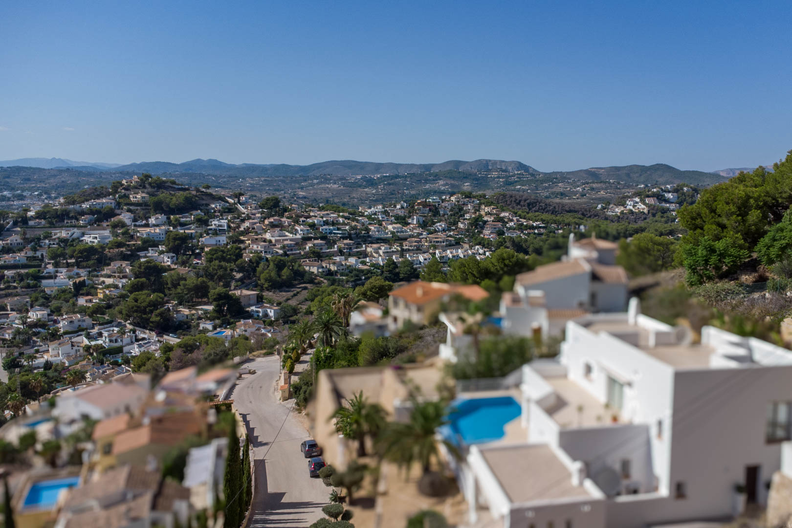 Elevated panoramic view of the El Portet residential area, showcasing white villas with private pools and distant mountain ridges under a clear sky.