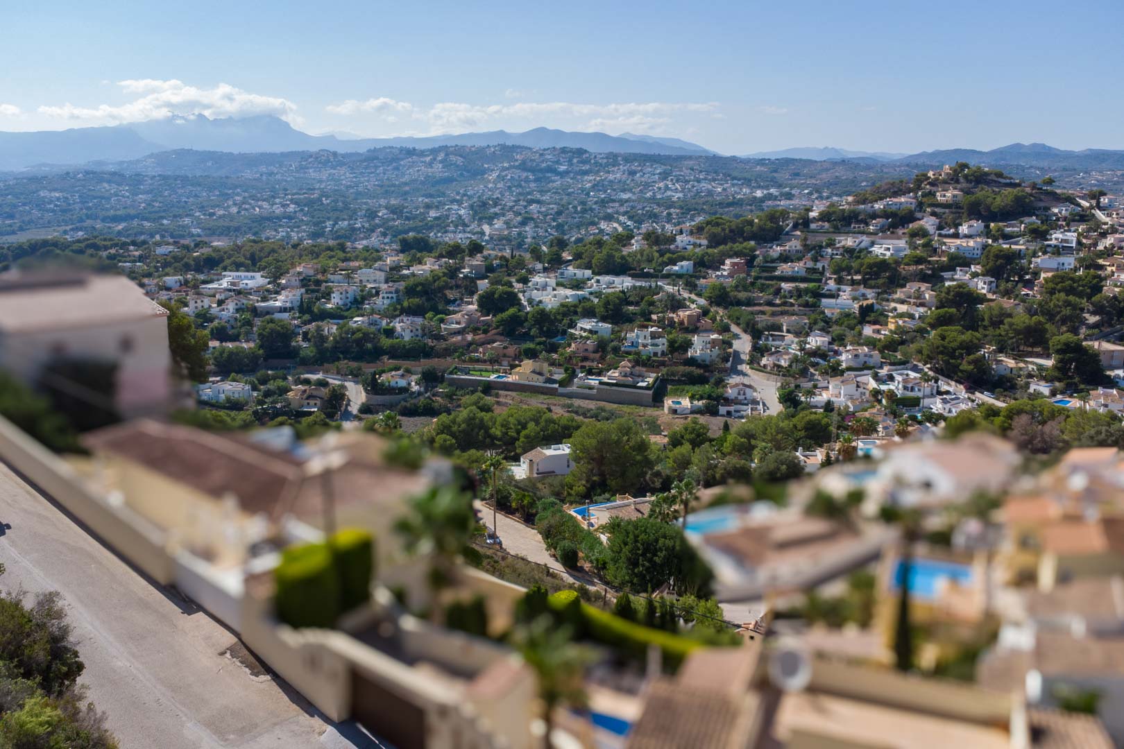 Elevated panoramic view over the El Portet residential area, featuring Mediterranean greenery and distant mountain ranges under a clear blue sky.