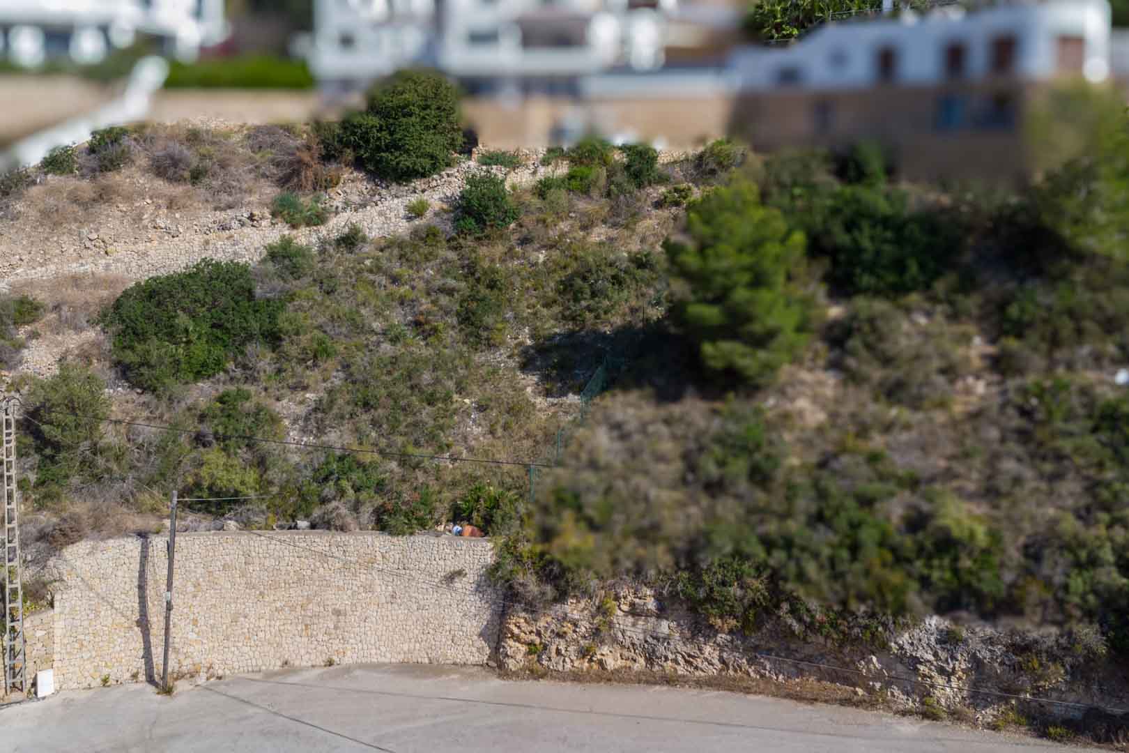 Elevated urban plot featuring natural stone retaining walls and Mediterranean vegetation, located within an established residential area.
