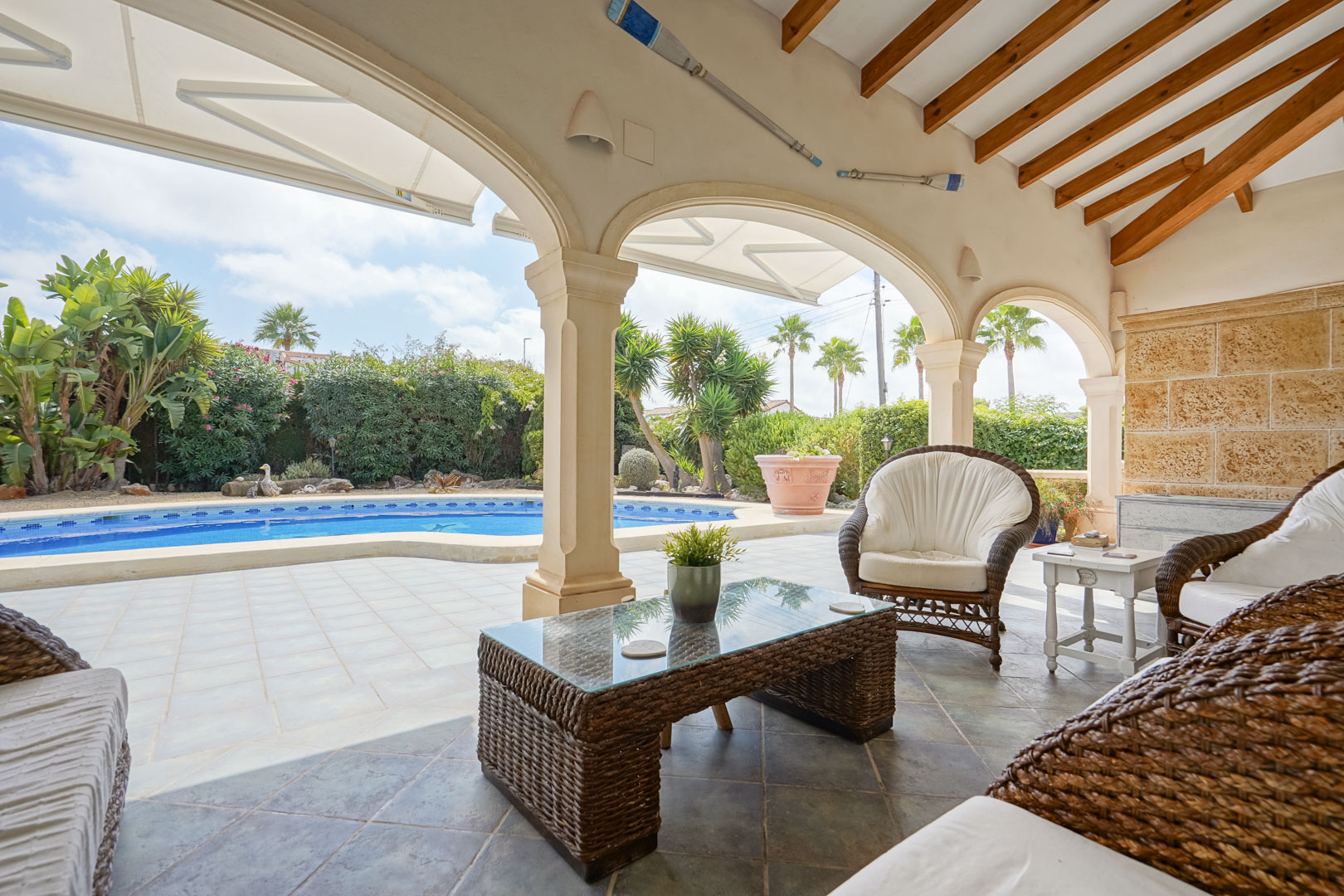 Covered terrace overlooking the pool. Features rattan furniture and a glass-topped coffee table.