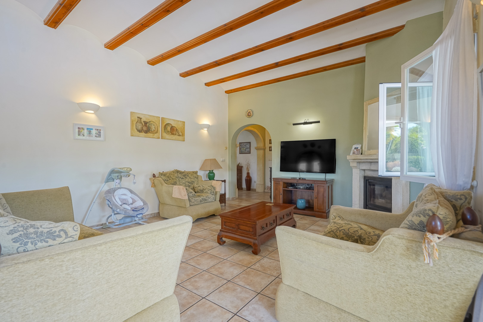 Living room with wood beams, stone fireplace, and tile floor. Classic furnishings and natural light.