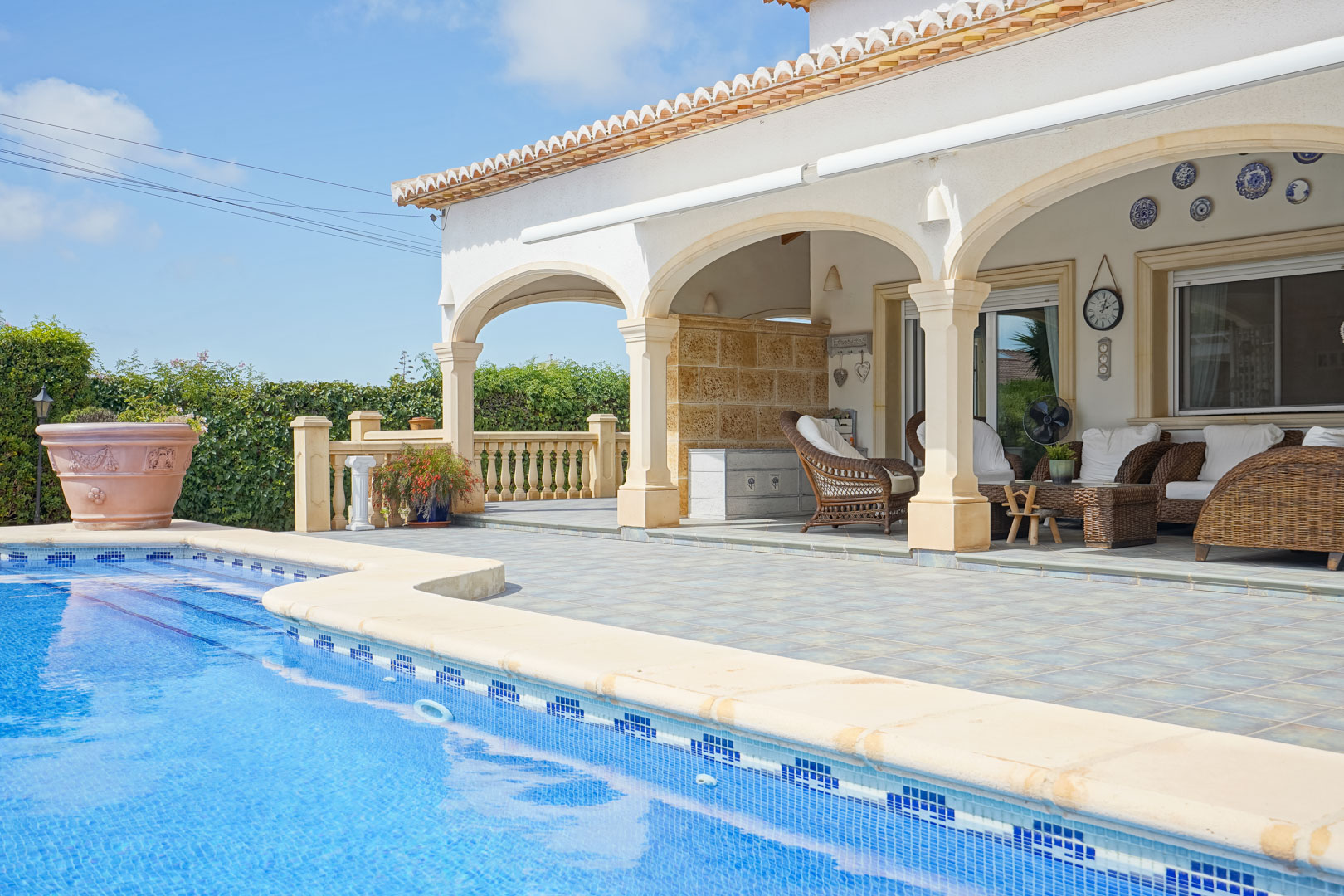 View of the pool and covered terrace with arches and wicker furniture in Jávea.