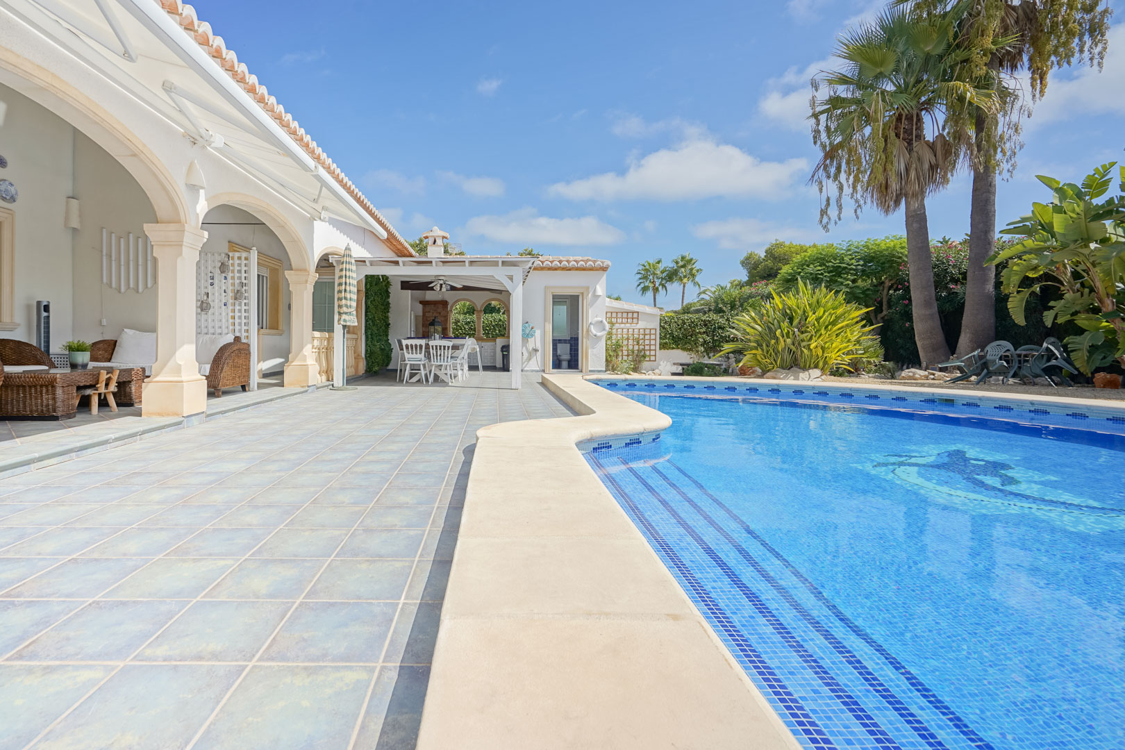 View of the pool with blue tiles and terrace with stone columns in Jávea.