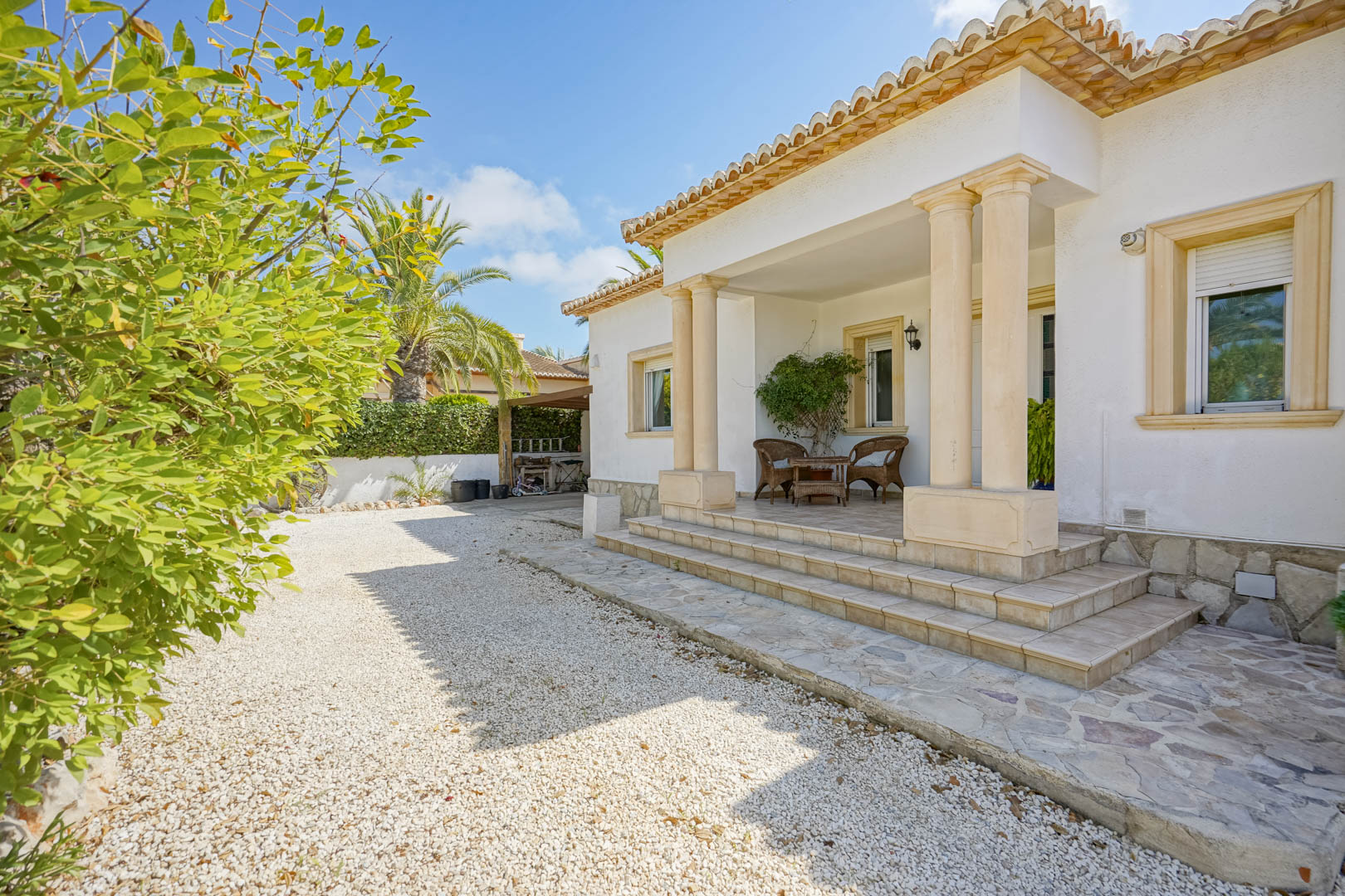 Villa entrance with white gravel, columned porch, and wicker furniture.