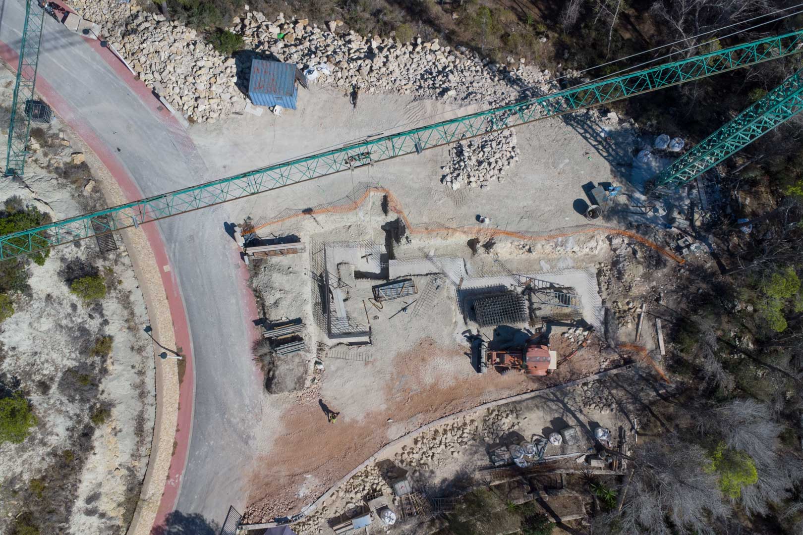 Aerial view of the initial construction phase, showing the foundation layout, steel reinforcement, and crane on the hillside plot.