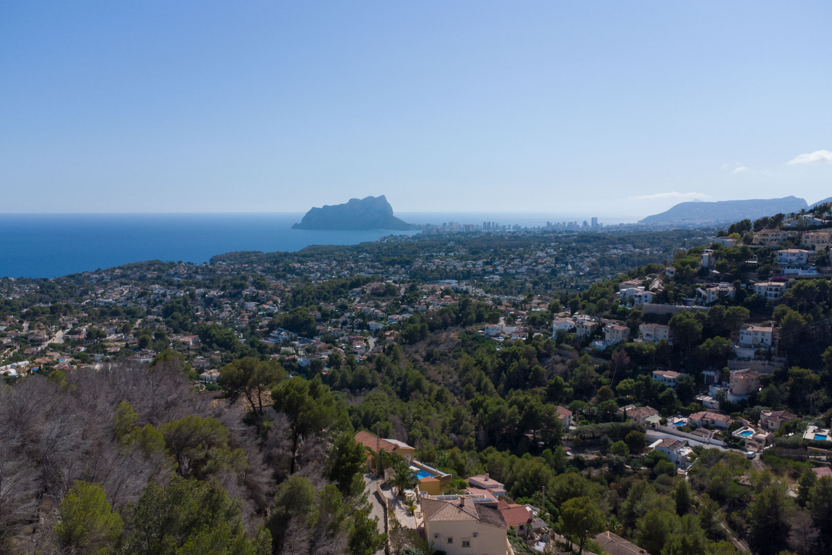 Elevated panoramic view overlooking the Mediterranean Sea and the Peñón de Ifach, showcasing the lush coastal landscape and residential hills.