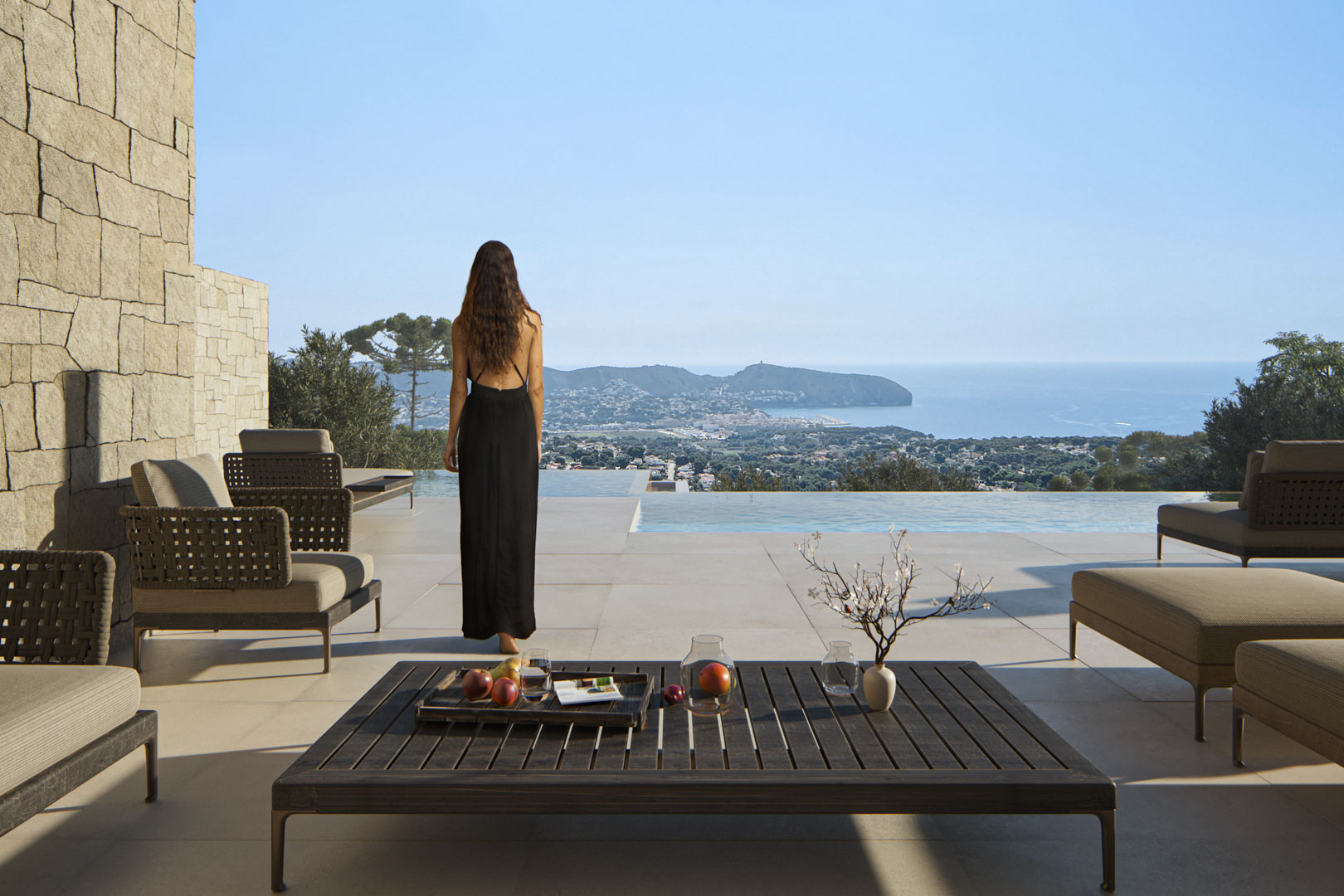 Outdoor terrace featuring designer lounge furniture, a natural stone wall, and an infinity pool with panoramic views of the Mediterranean Sea and Moraira.