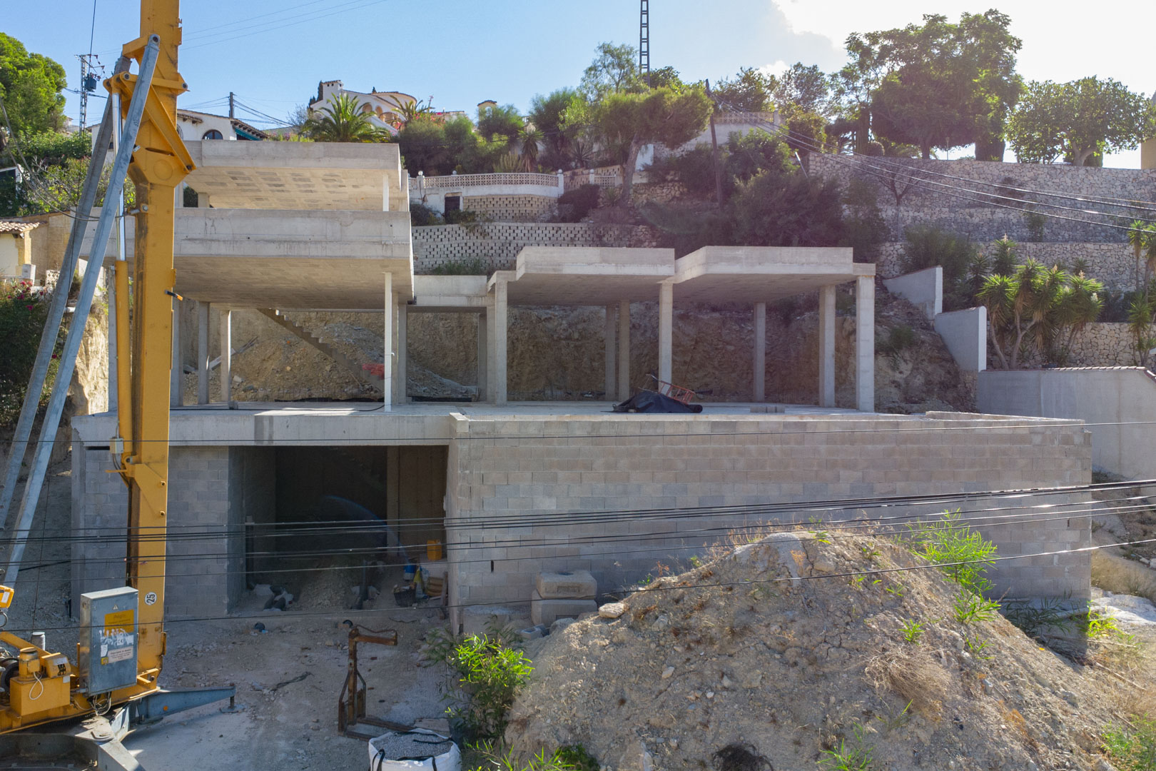 Exterior view of the villa's reinforced concrete structure under construction in San Jaime, showing the three levels and the integrated garage area on a sloped plot.