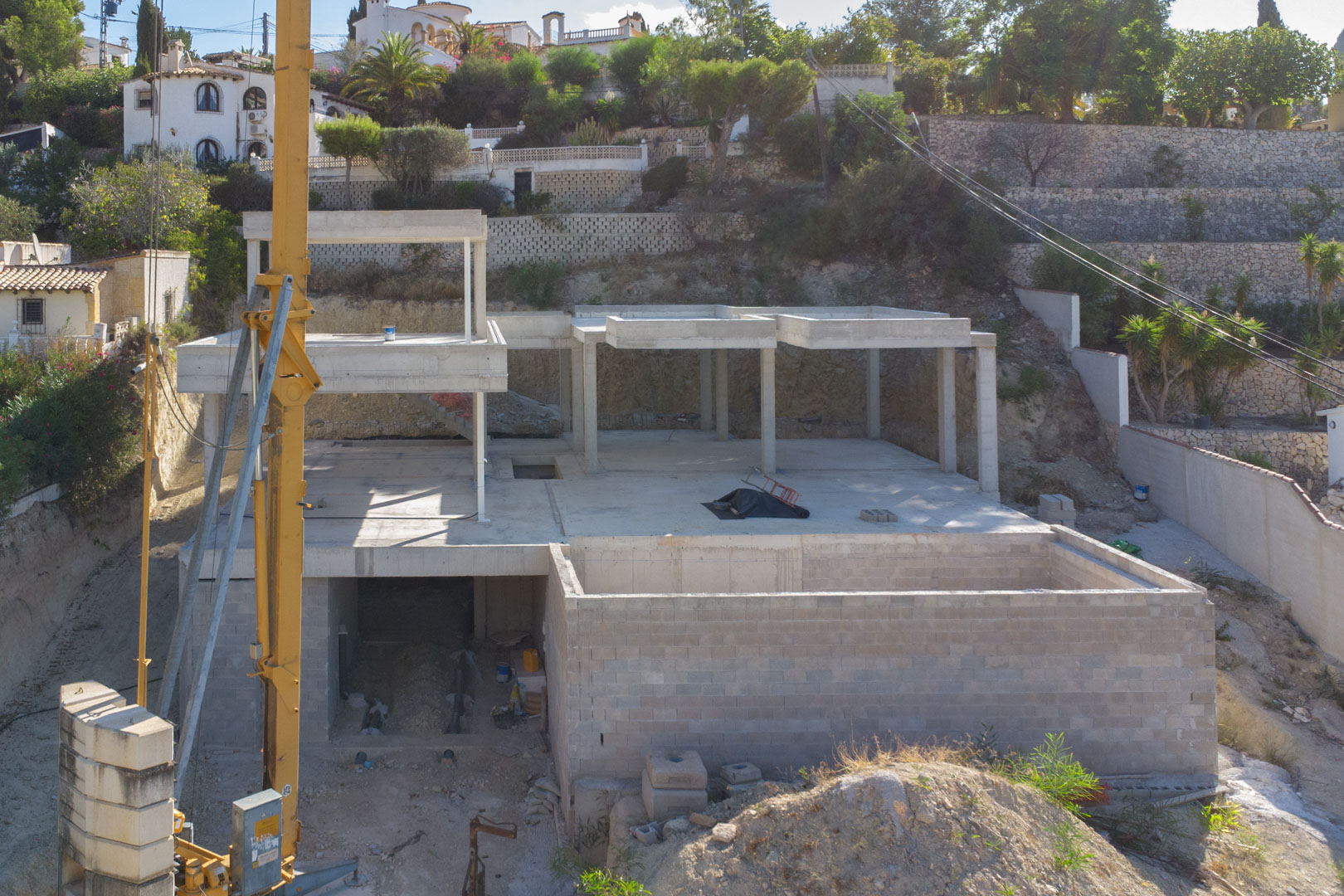 View of the reinforced concrete structure under construction, showcasing the multi-level layout and the integrated hillside stone retaining walls.