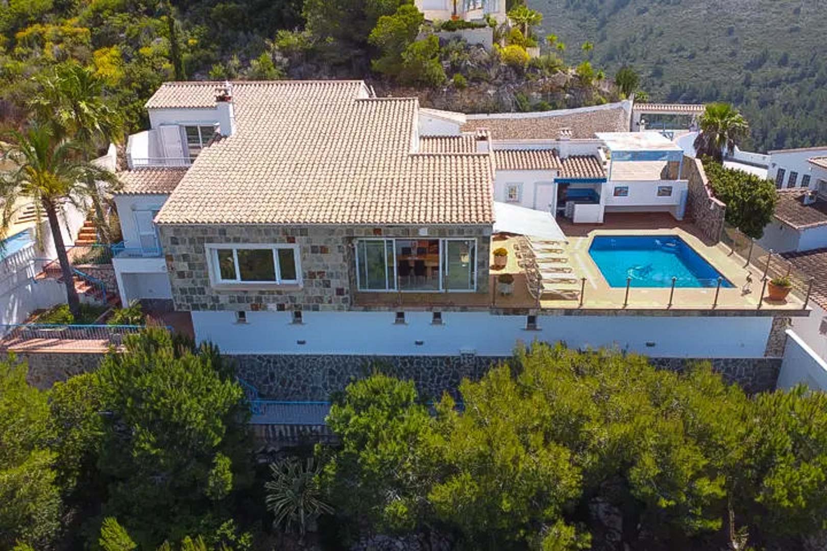 Aerial view of the villa featuring natural stone masonry, traditional tiled roofs, and an elevated terrace with a private pool and sun deck.