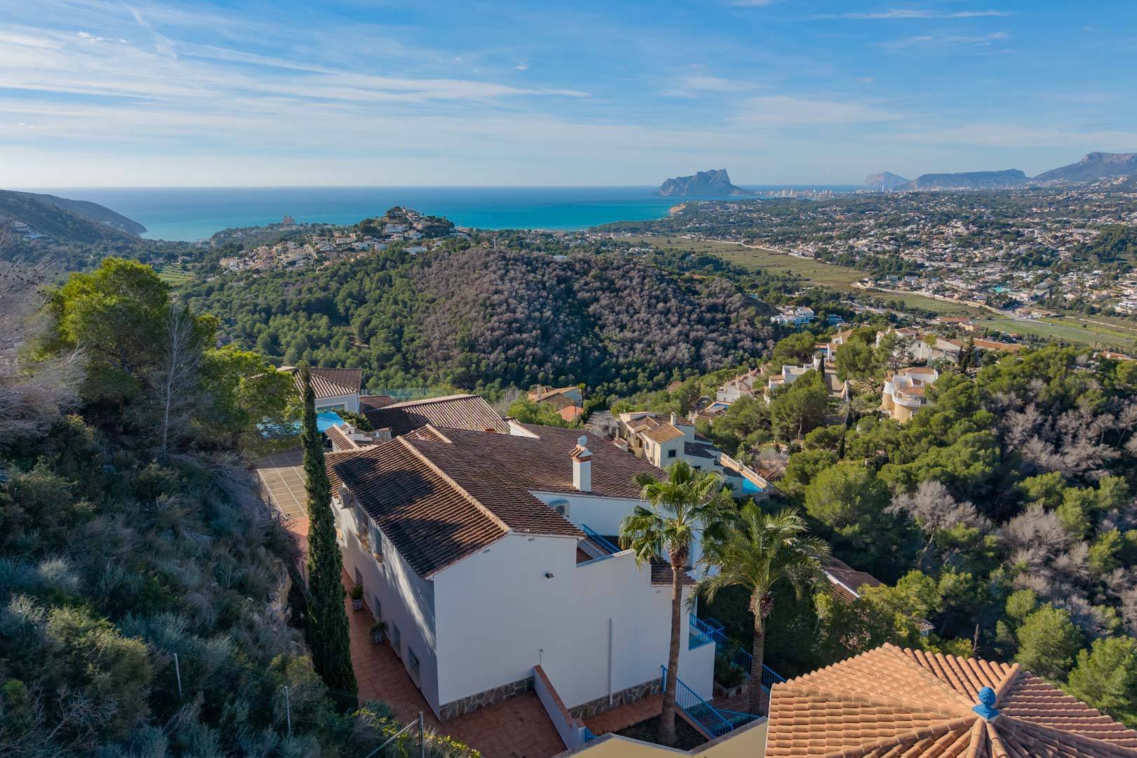 Elevated view of the villa featuring terracotta roofing, nestled in a pine forest with expansive views of the Mediterranean coast and Peñón de Ifach.