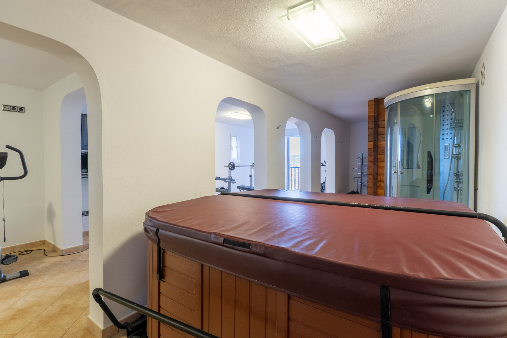 Indoor wellness area featuring a covered hot tub, a hydromassage shower cabin, and arched entryways leading to a private home gym.