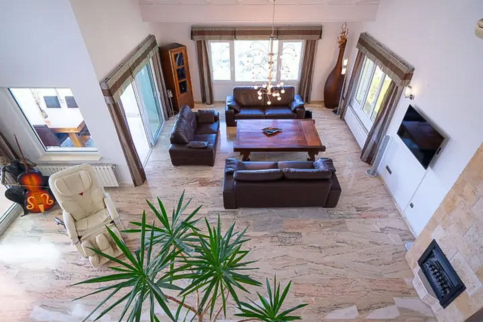 Open-plan living area featuring marble floors, a stone-clad fireplace, brown leather sofas, and a large wooden coffee table under a modern chandelier.