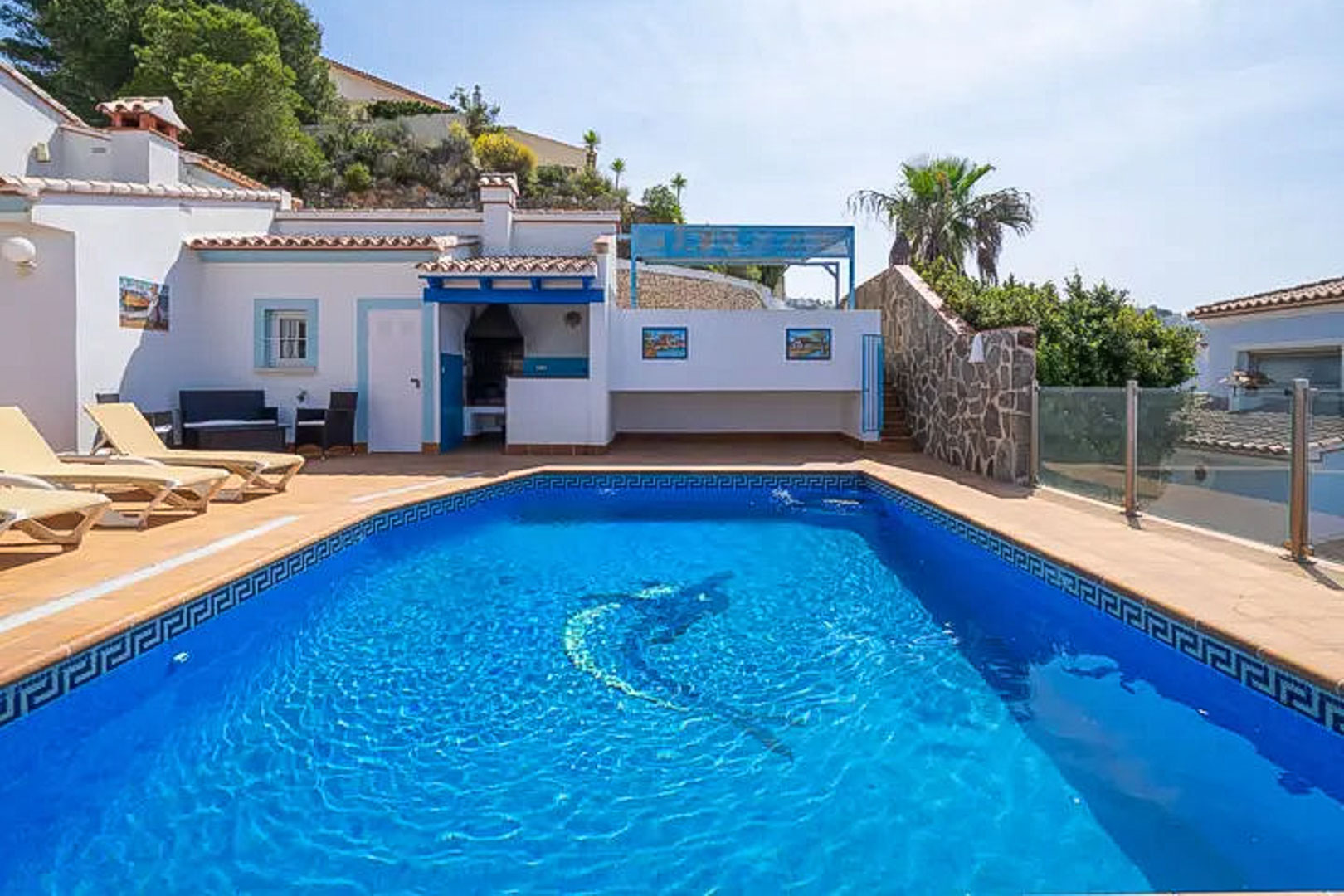 Outdoor pool featuring a dolphin mosaic and Greek key tiling, accompanied by a sun terrace, built-in barbecue area, and traditional blue and white architecture.