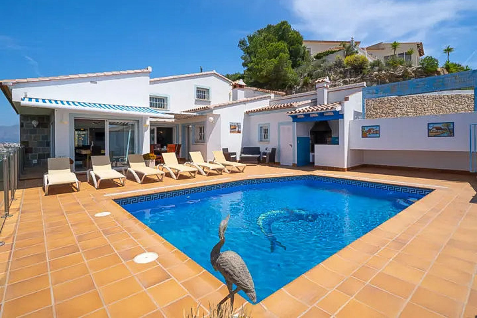 Outdoor pool featuring a dolphin mosaic and sun loungers on a terracotta terrace, adjacent to the white villa with its integrated BBQ area.