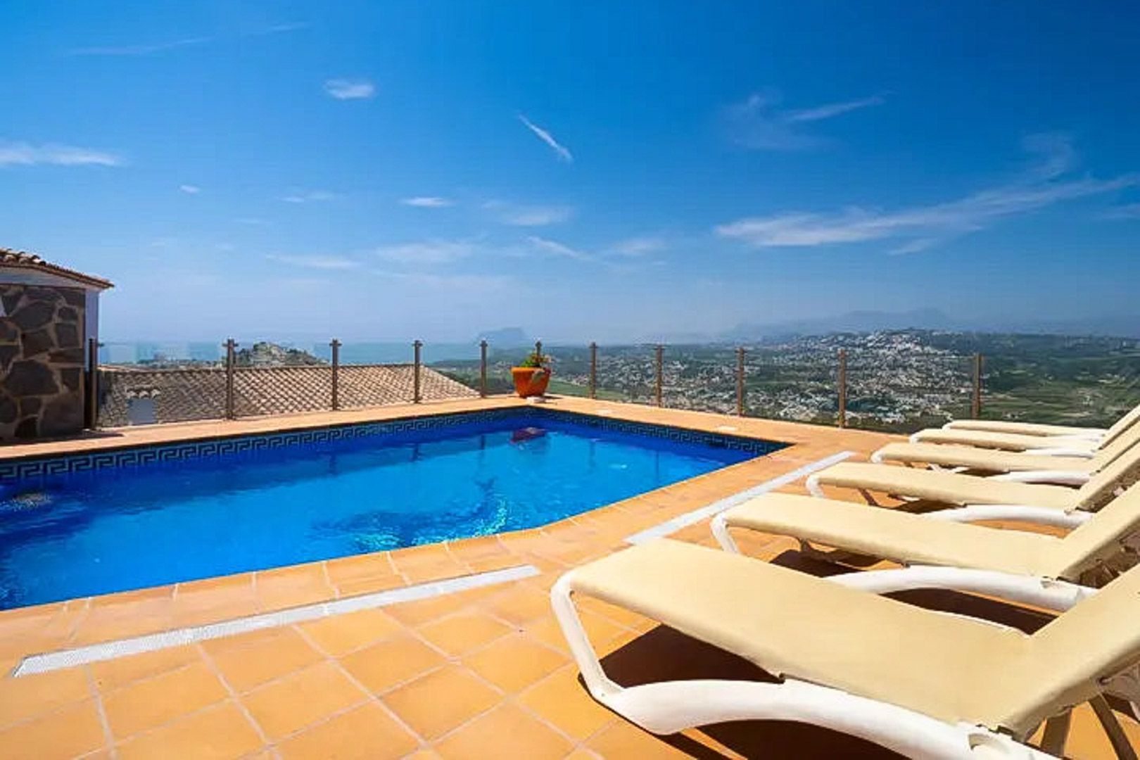 Outdoor swimming pool featuring a Greek key border, terracotta sun deck with loungers, and a glass railing overlooking the Mediterranean Sea and Moraira.