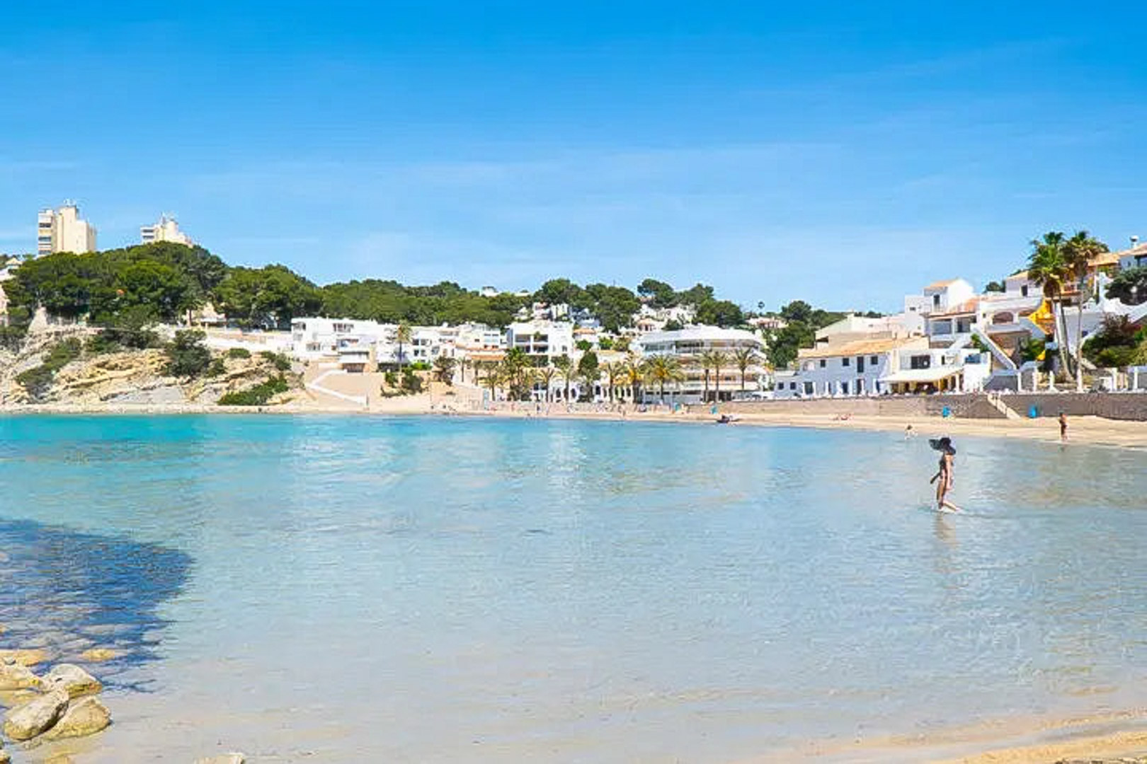 Panoramic view of El Portet beach in Moraira, featuring shallow turquoise waters and traditional white Mediterranean buildings along the coastline.