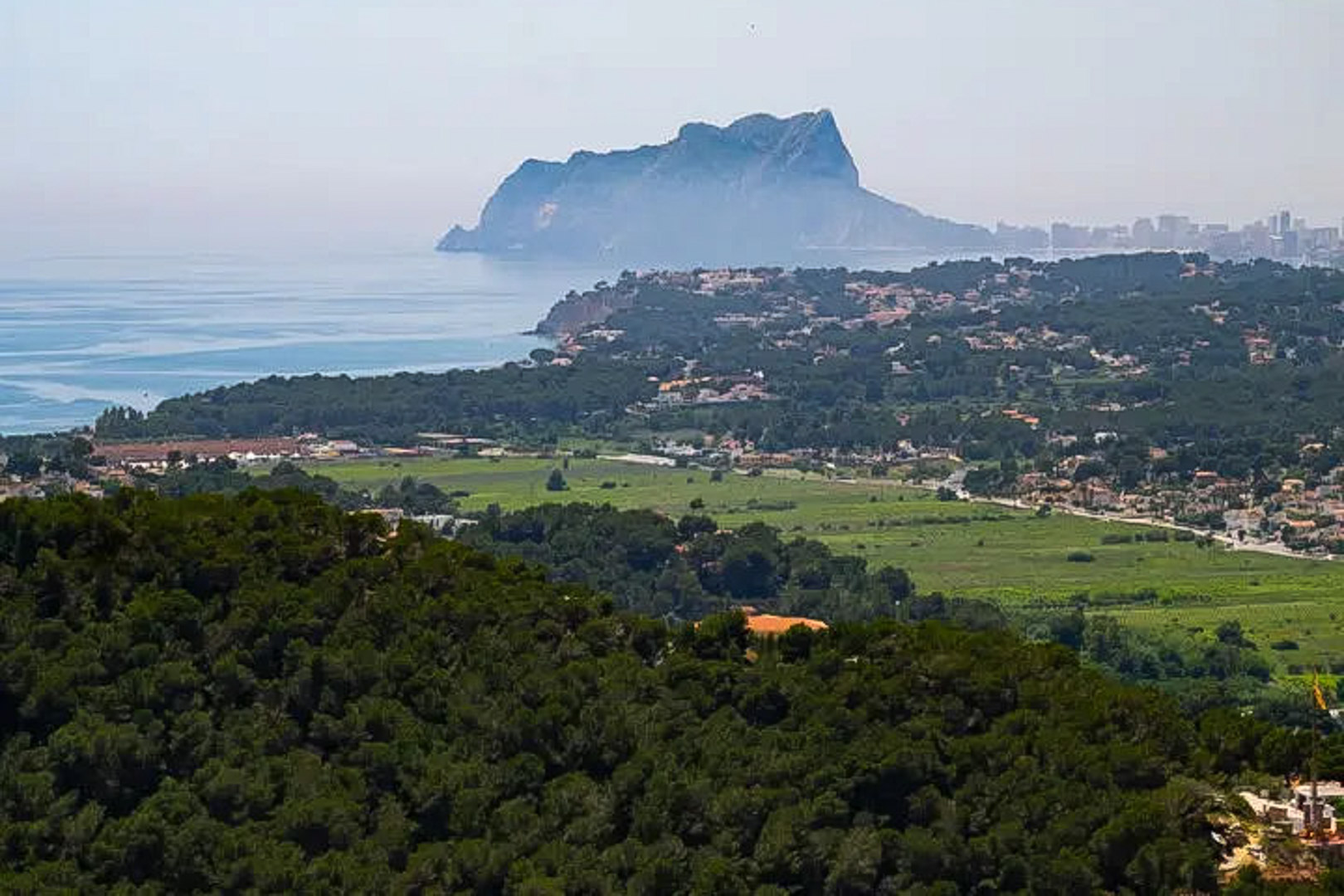 Panoramic views towards the Peñón de Ifach and the coastline, highlighting the contrast between dense pine forests and the blue Mediterranean Sea.