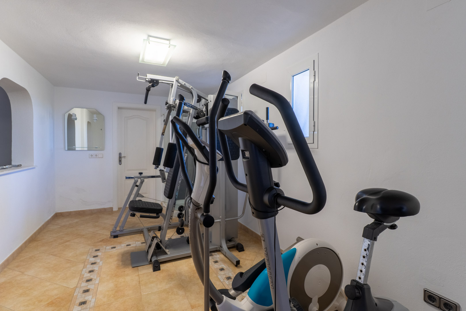 Private home gym featuring a multi-station weight machine, elliptical trainer, and stationary bike on tiled flooring.